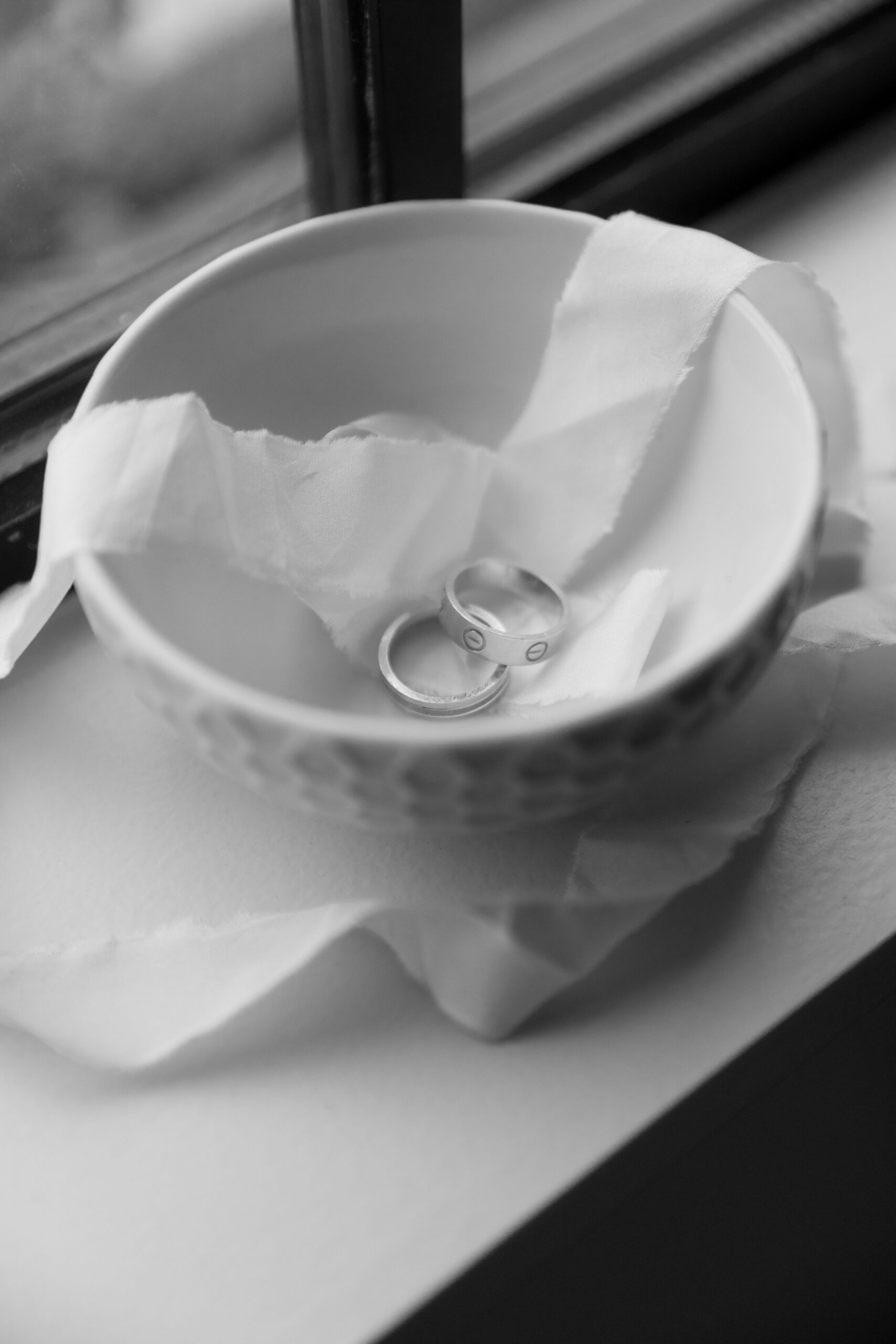 black and white photo of Cartier wedding bands in small dish with ribbon on window ledge