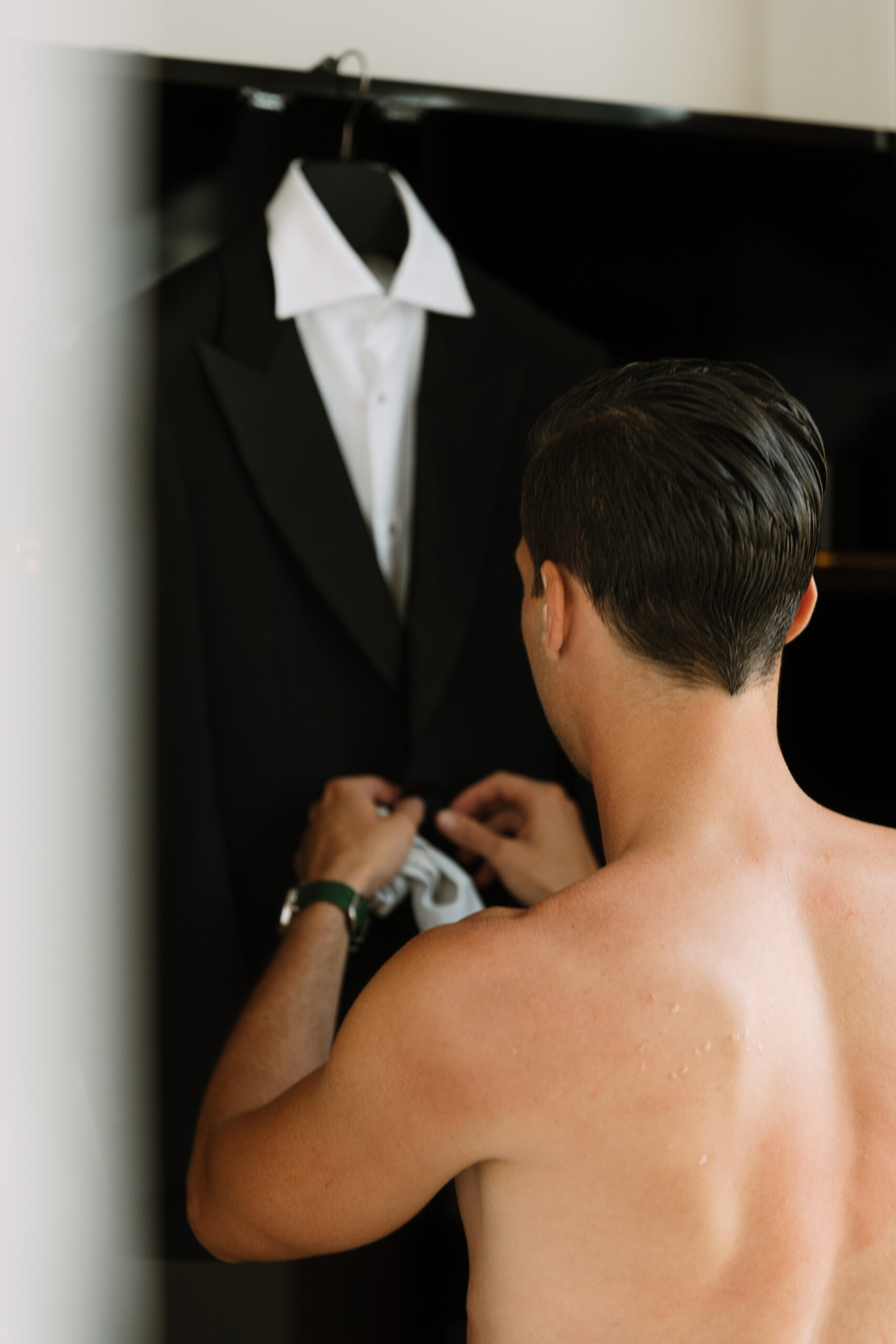 shirtless groom pulling his tux out of the wardrobe