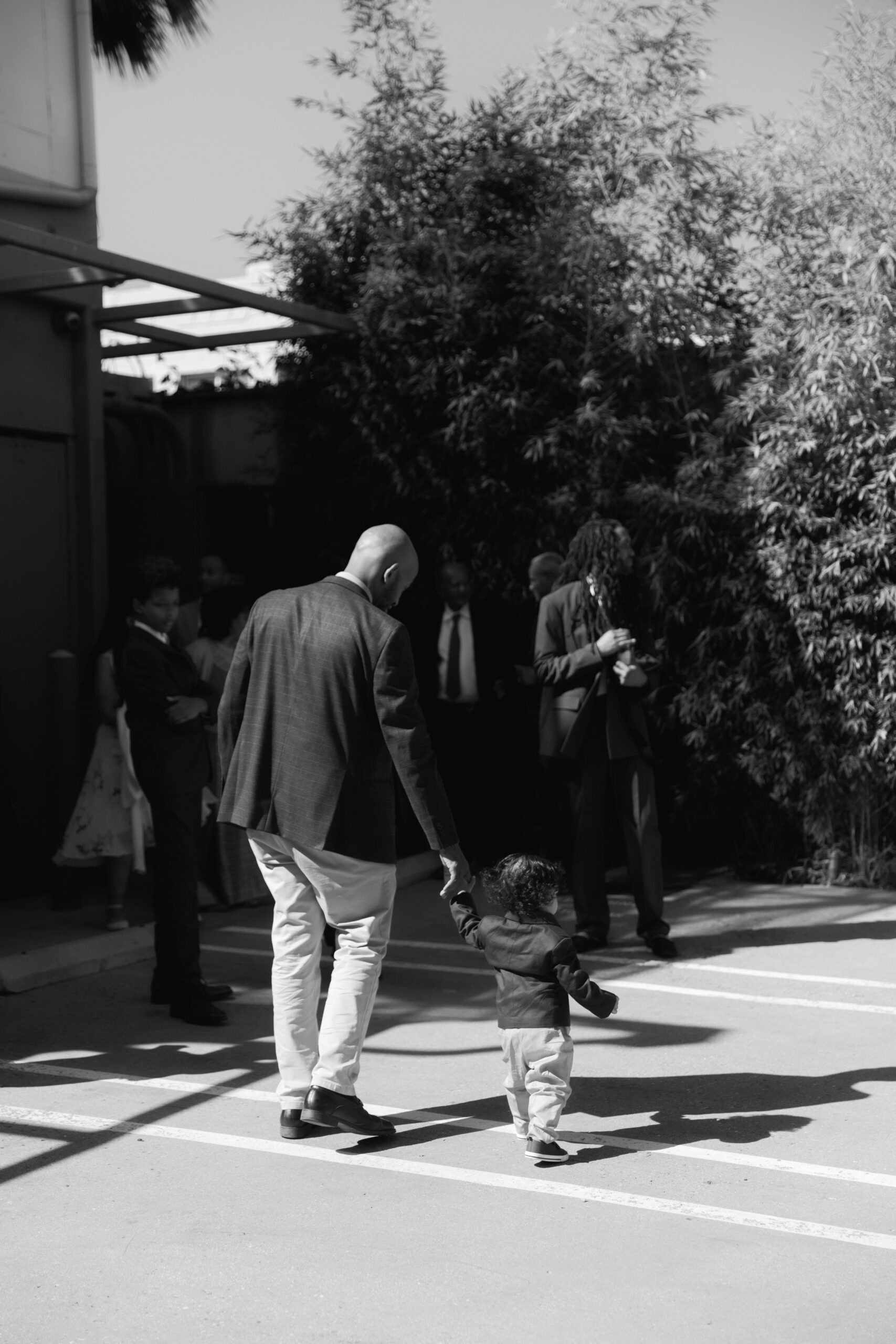 black and white photo of father holding baby's hand as they walk into wedding reception