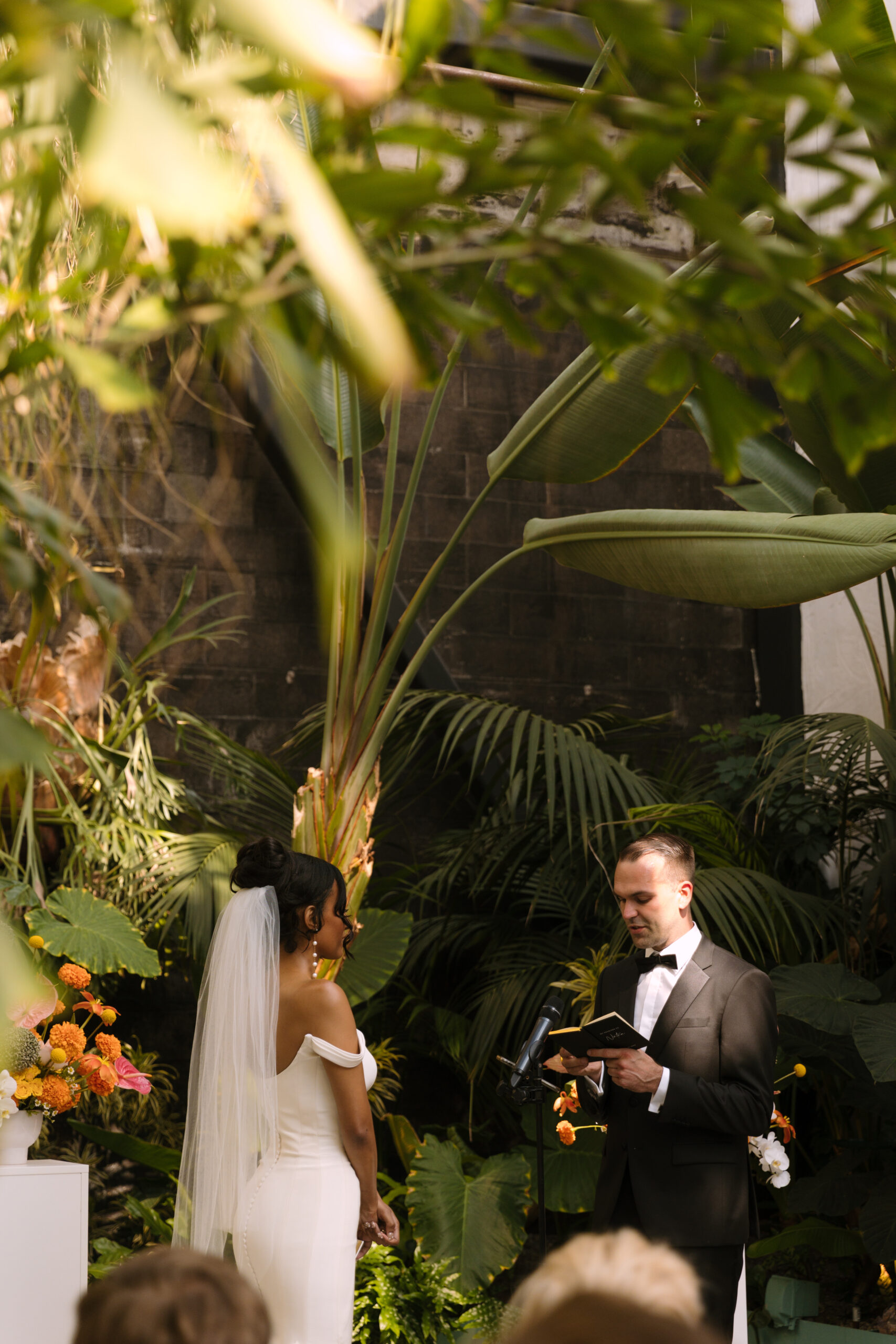 wide portrait of bride and groom exchanging wedding vows in tropical ceremony space at the Grass Room DTLA