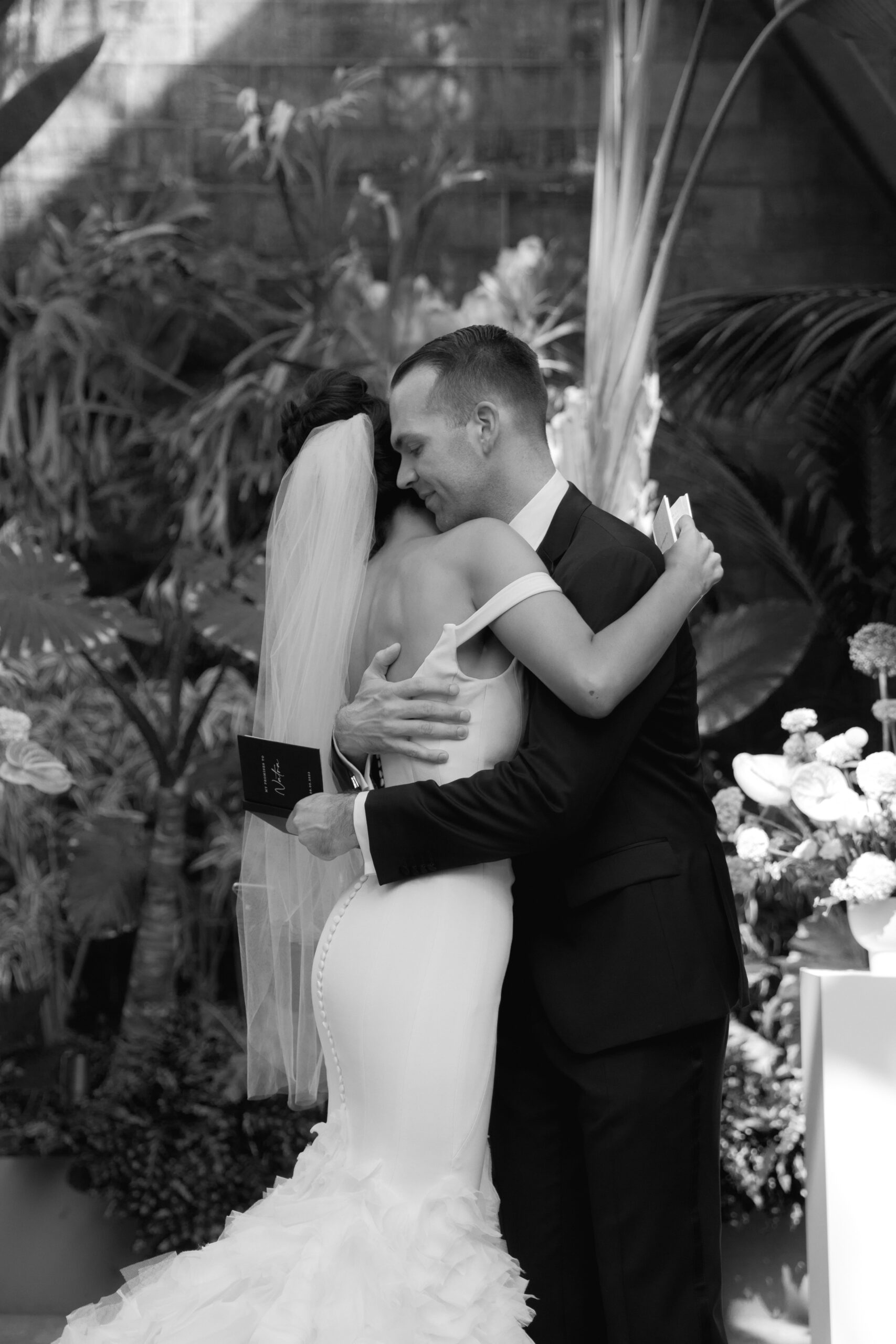 black and white photo of bride and groom hugging while still holding wedding vow books