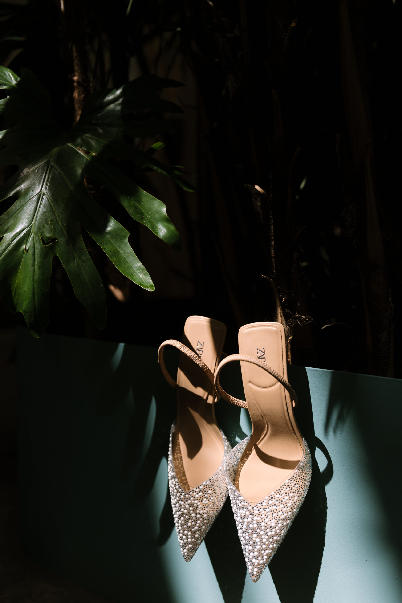 Zara pearl heeled slingbacks hung on turquoise wall under shadow of monstera leaf