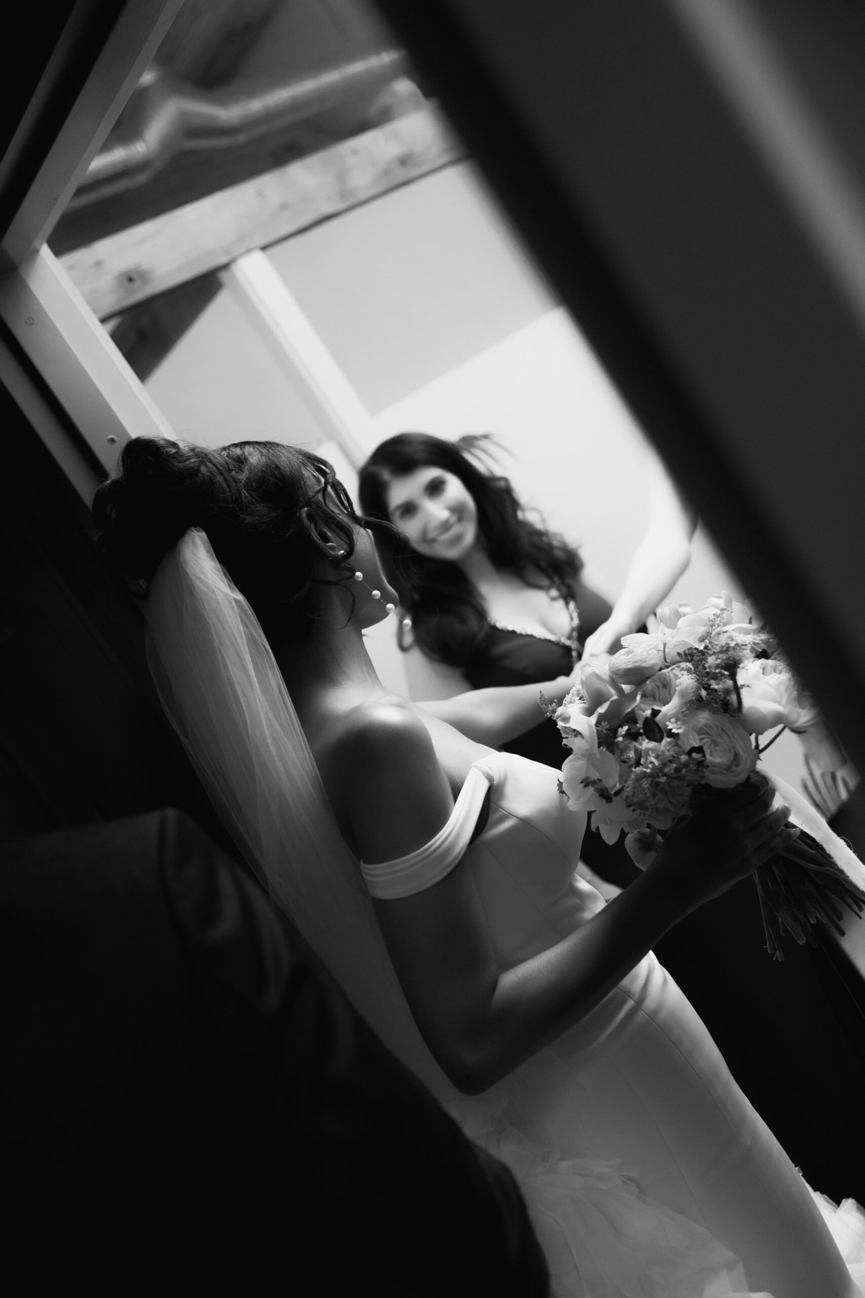 black and white photo of bride looking through doorway at her friend during cocktail hour