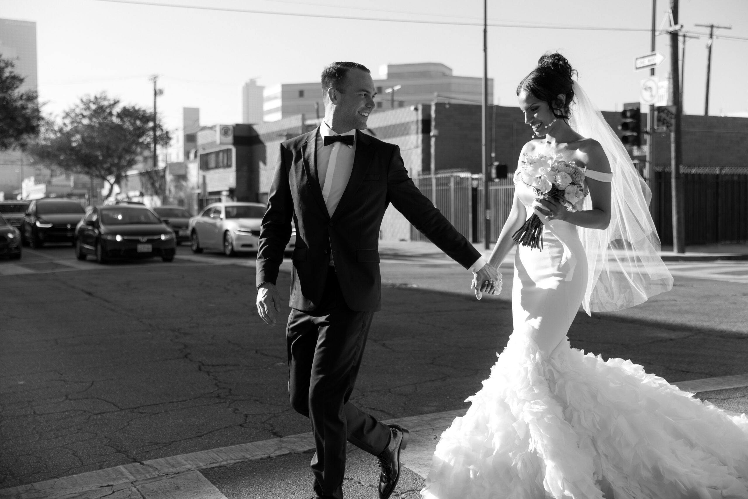 black and white photo of bride and groom holding hands as they walk through crosswalk in DTLA