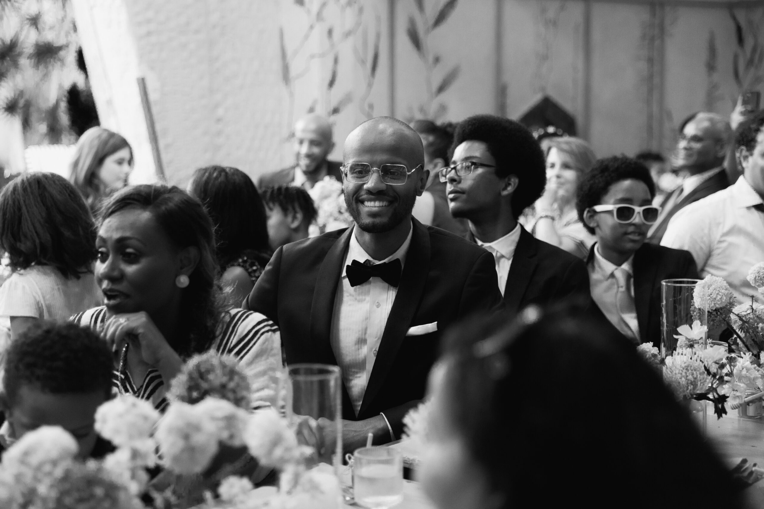 black and white photo of bride's brother sitting with family members during wedding reception