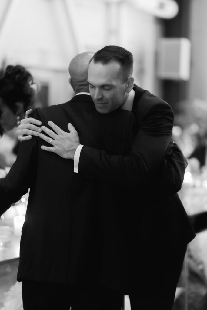 black and white photo of groom hugging his new father in law after toasts