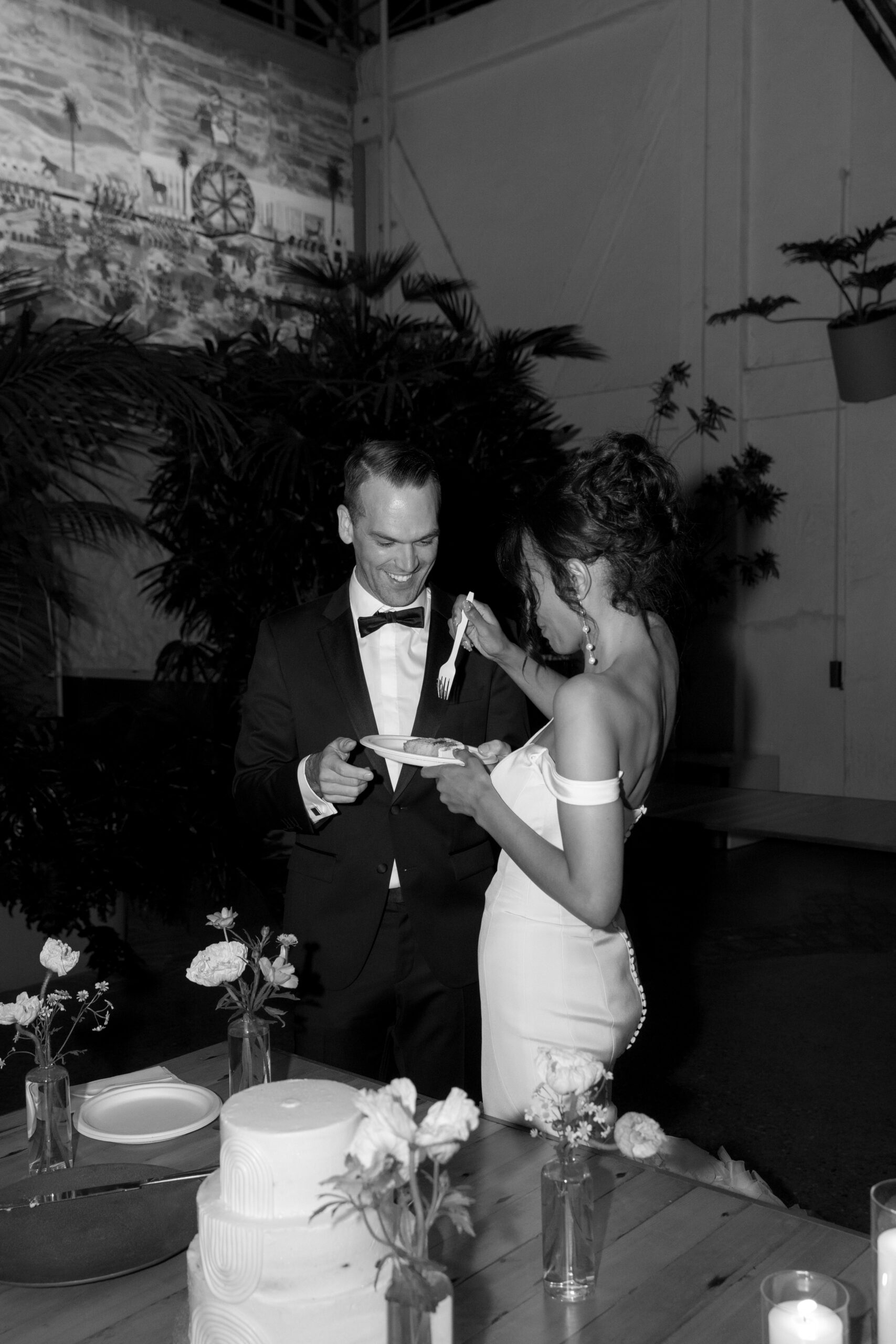black and white photo of bride about to feed a bite of cake to her groom