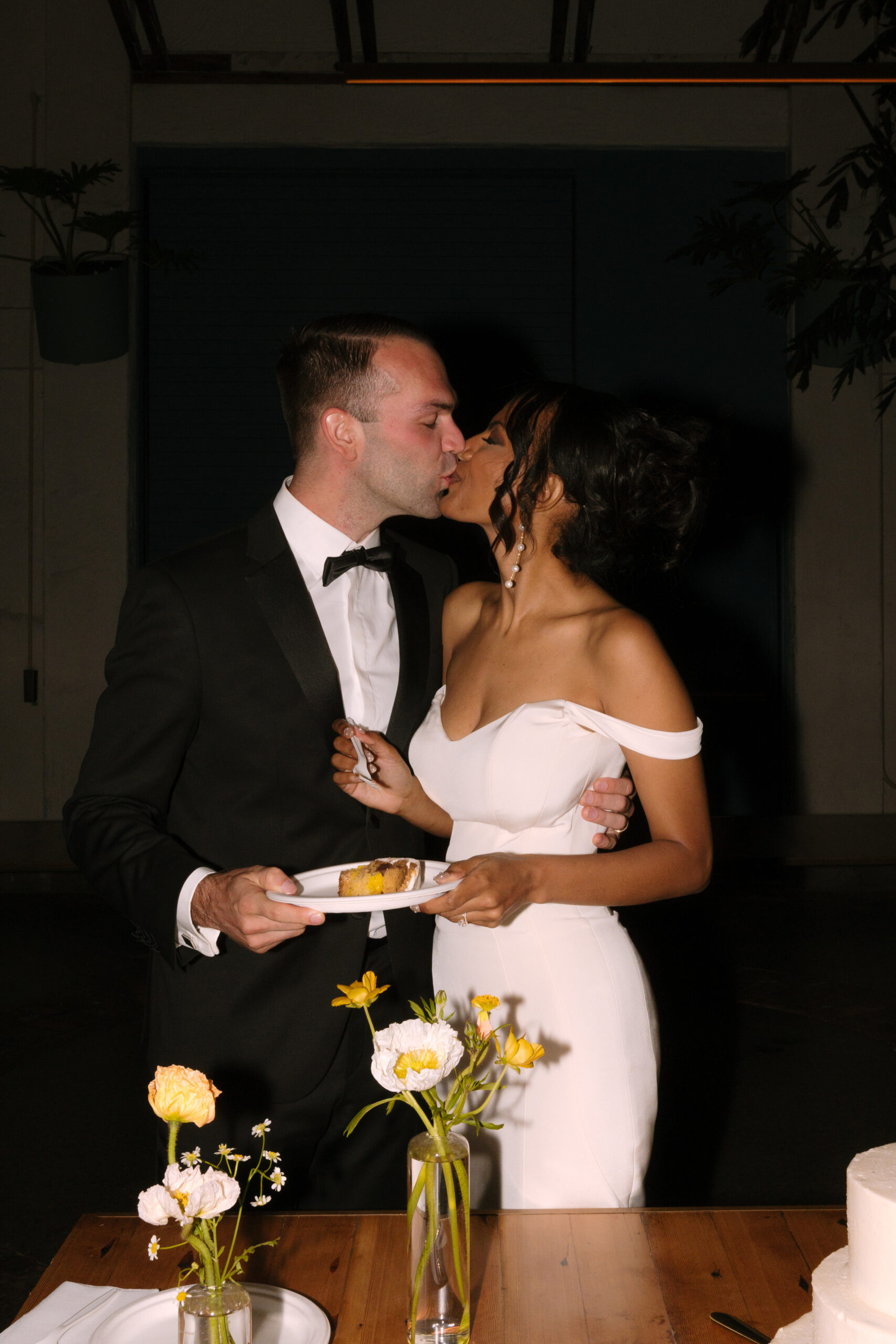 direct flash photo of bride and groom kissing after sharing a bite of their wedding cake