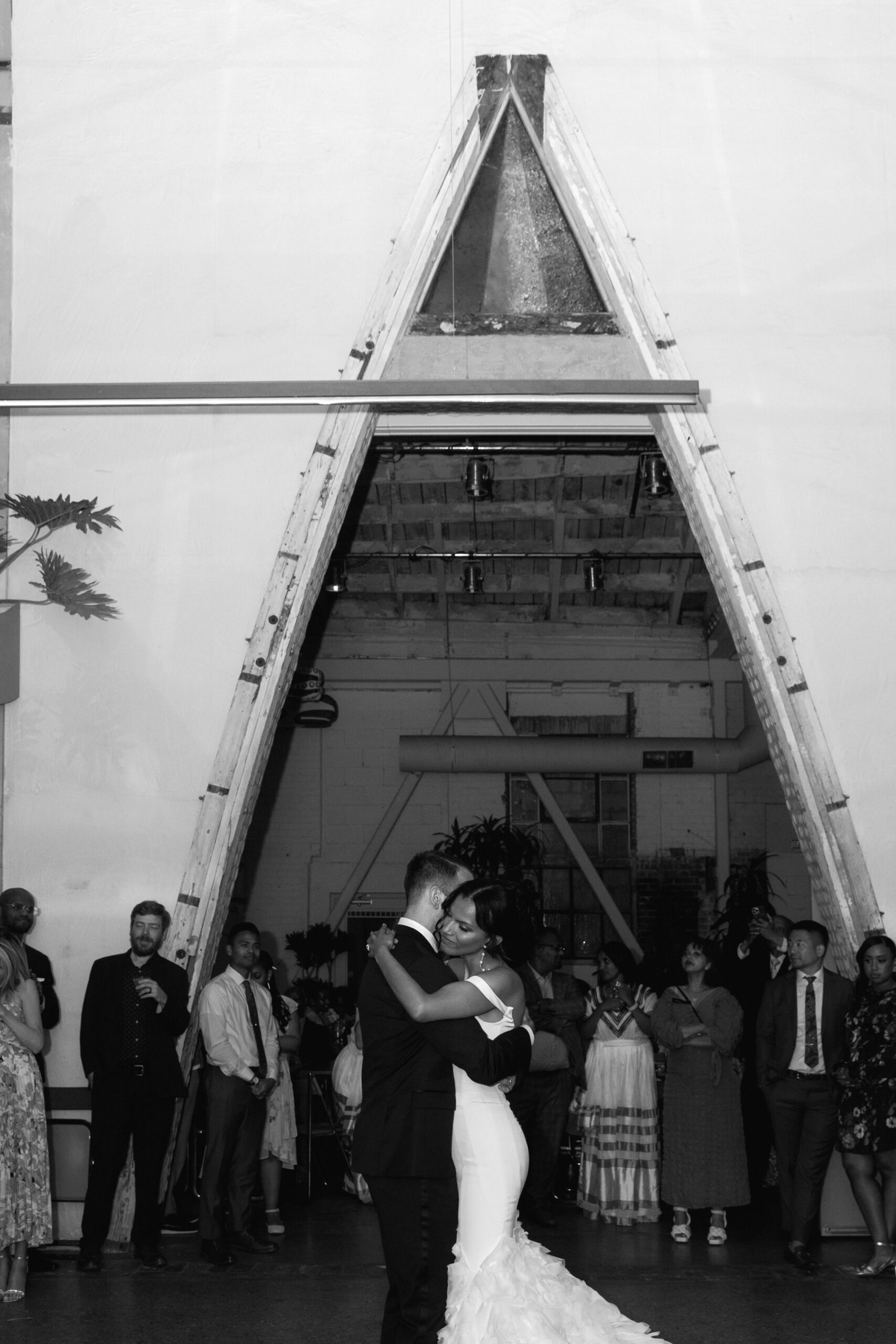 wide black and white flash portrait at Grass Room DTLA of bride and groom embracing during first dance while guests watch