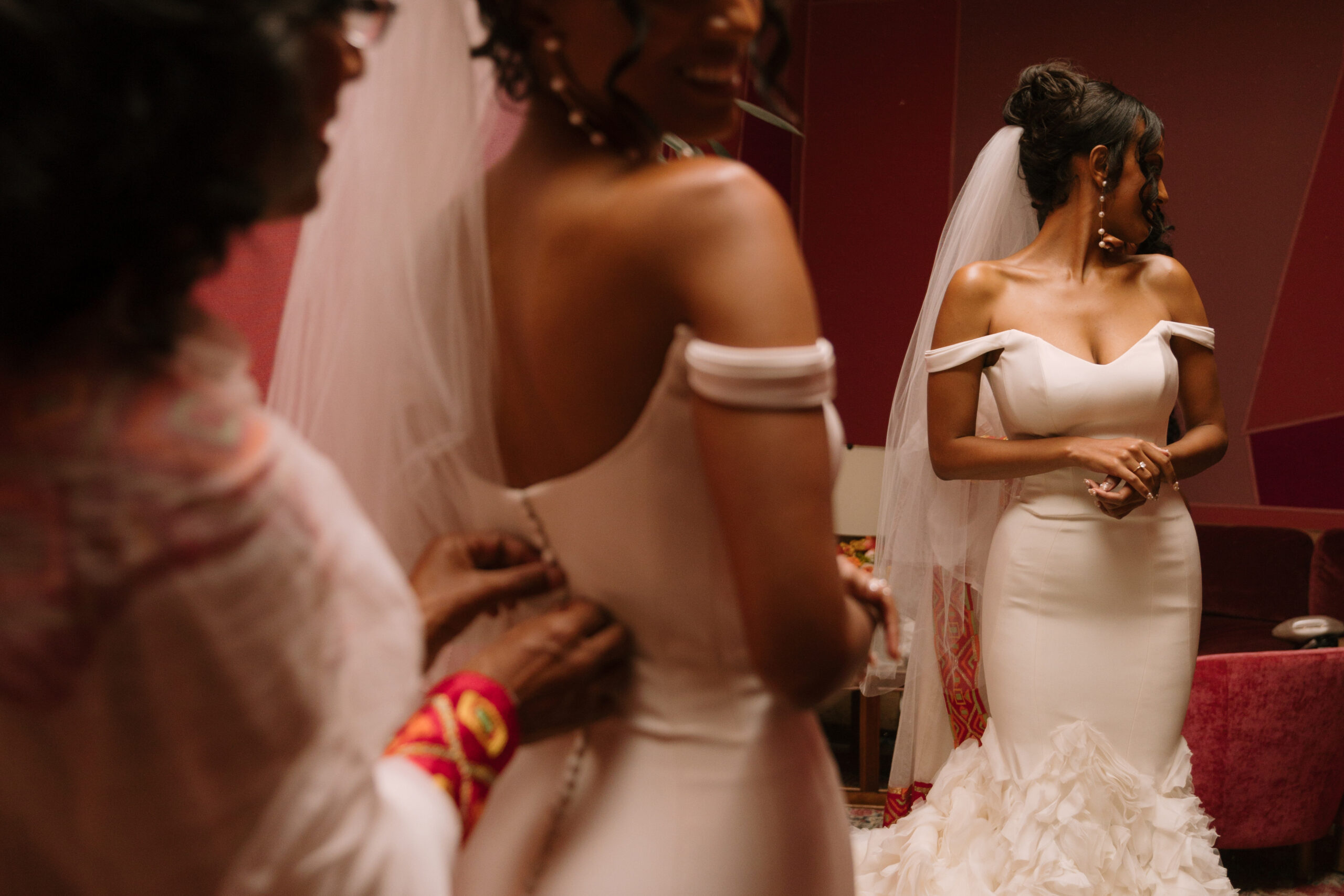 close up of Ethiopian mom zipping her daughter into Ines di Santo wedding gown in red bridal suite