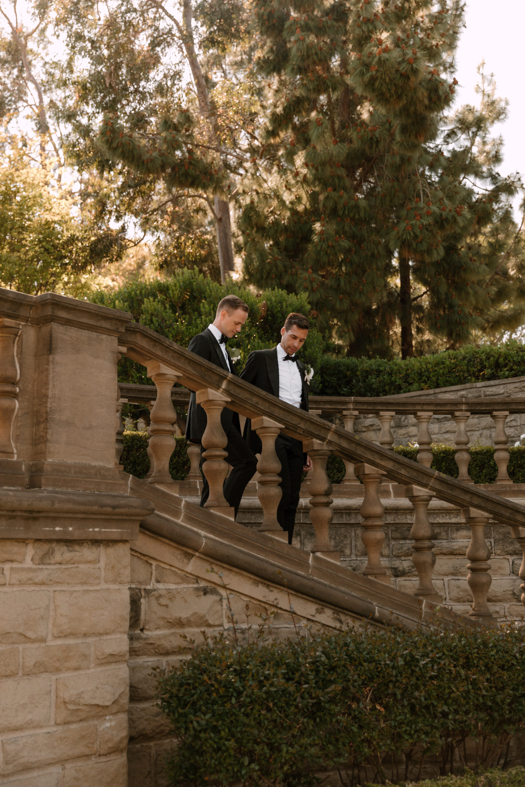 gay couple walking and holding hands down garden staircase overlooking Greystone mansion