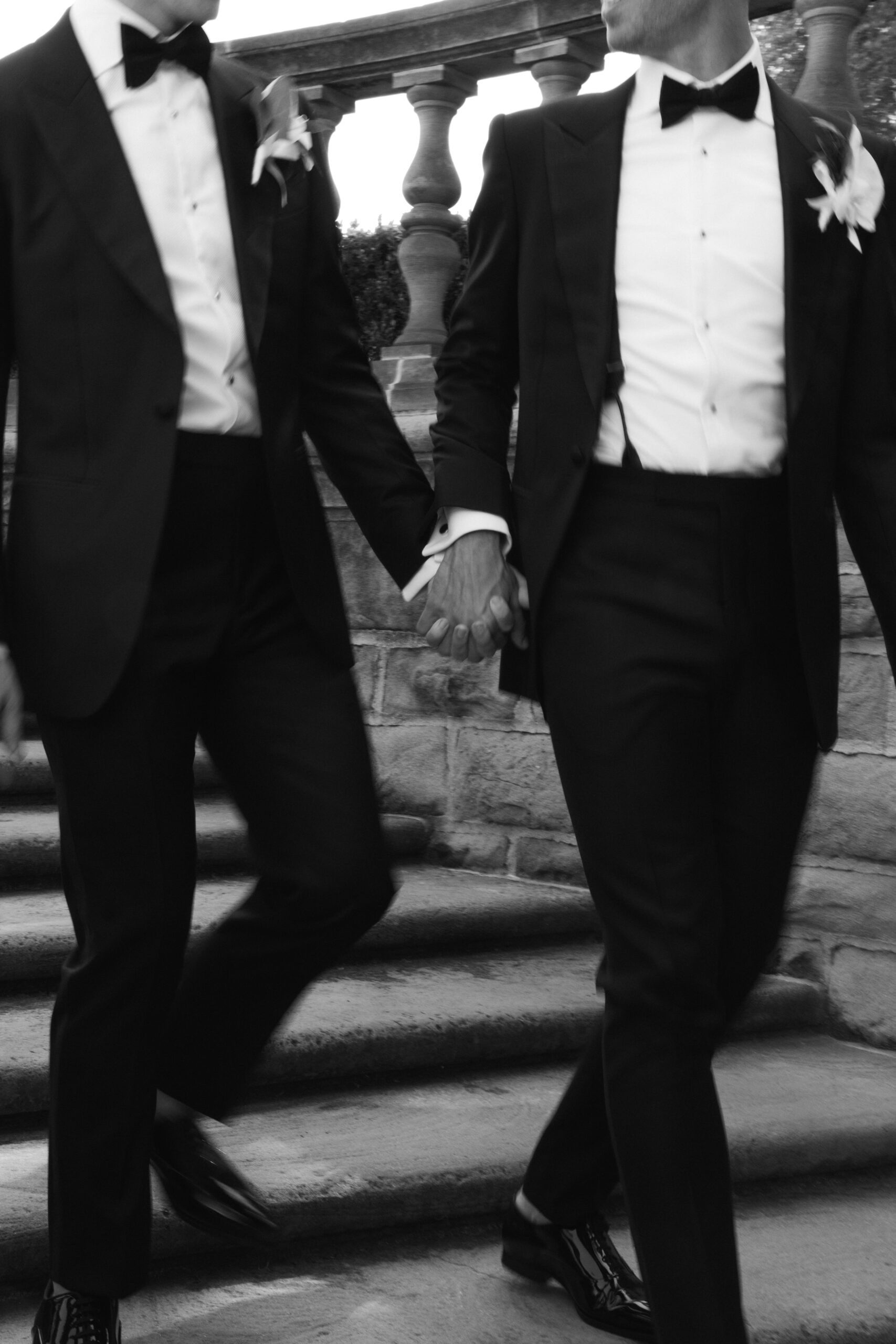 blurry movement black and white closeup of gay couple walking and holding hands down garden staircase overlooking Greystone mansion