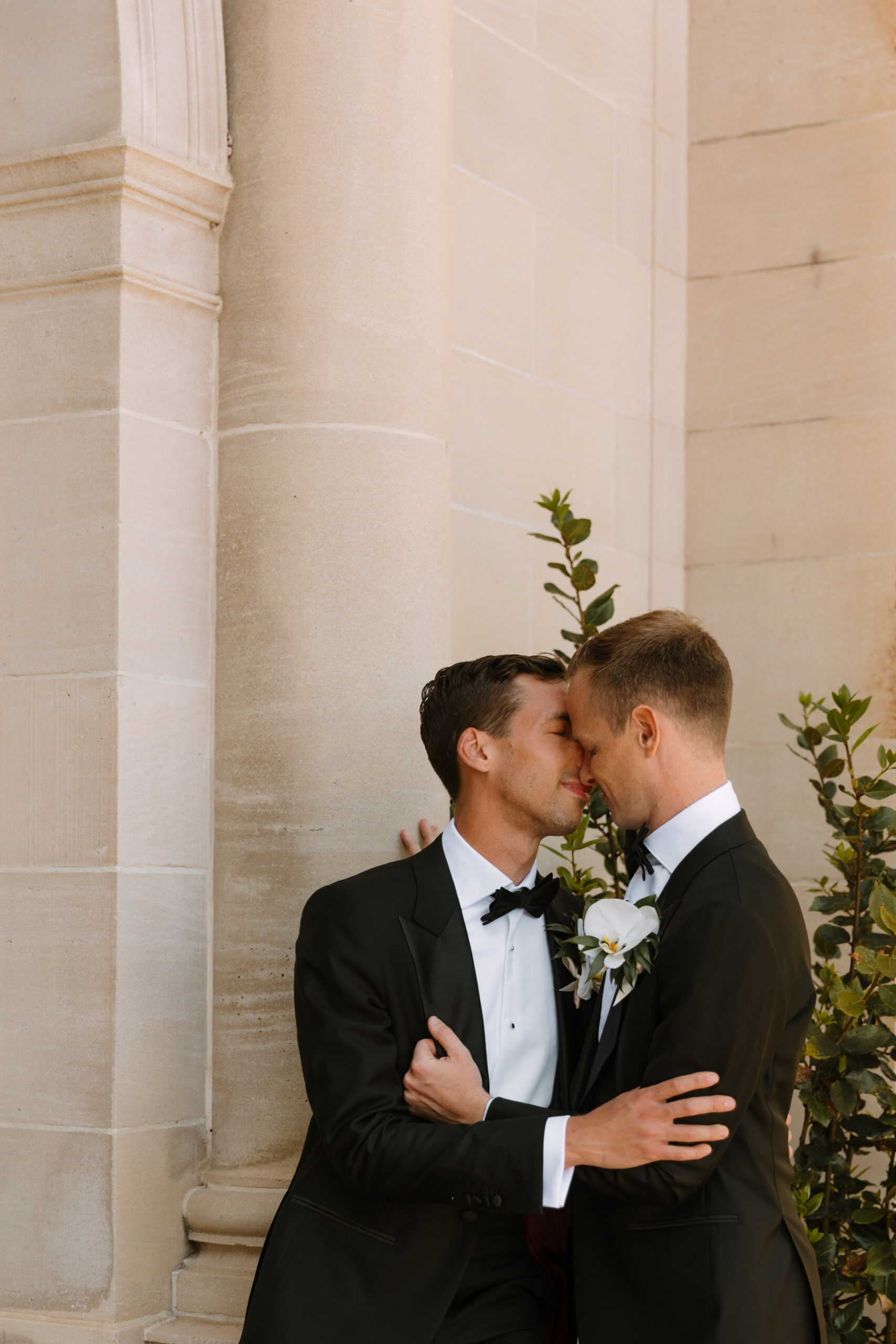 gay couple leans in close for embrace in front of wall at Greystone Mansion