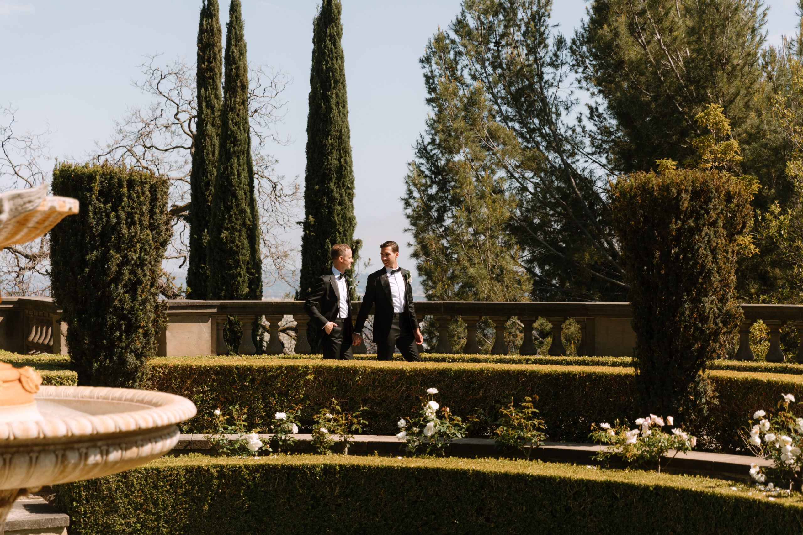 gay couple holding hands as they walk through fountain garden at Greystone Mansion