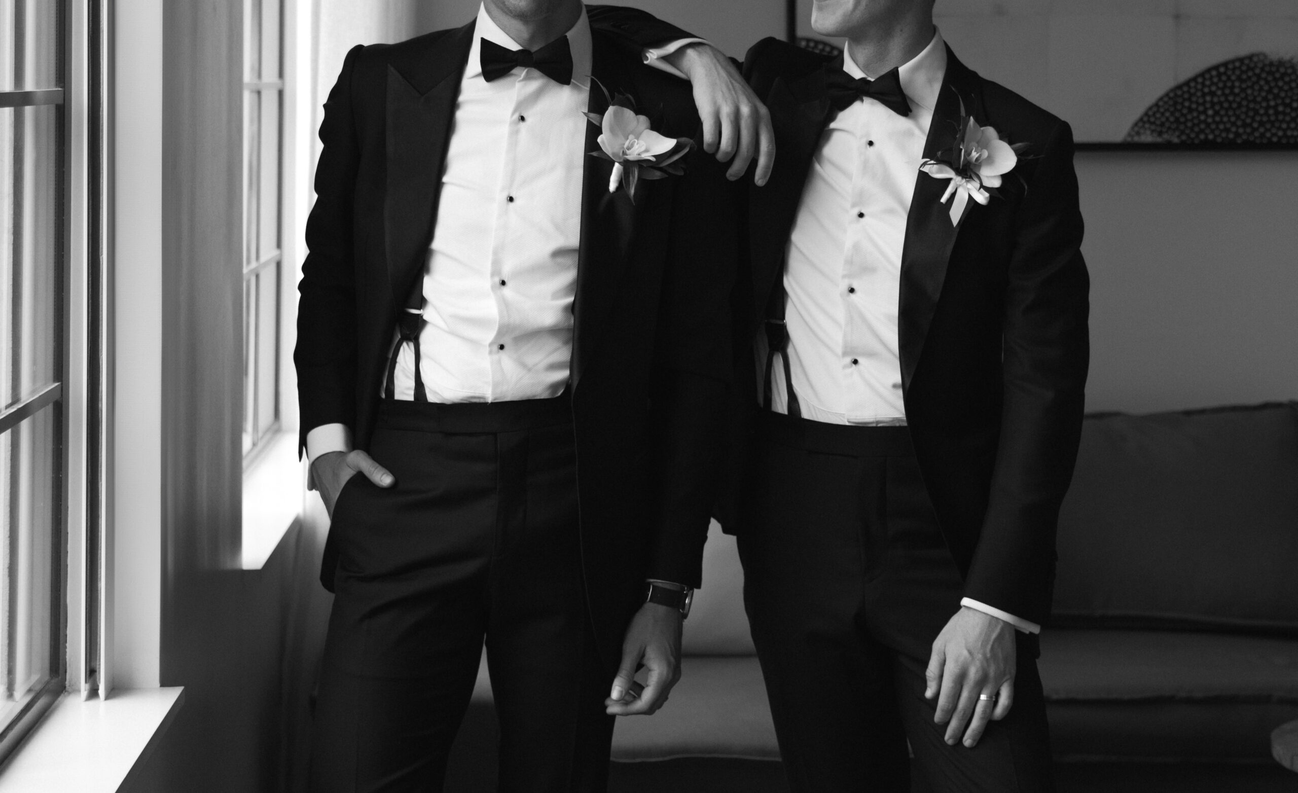 black and white closeup of gay couple posing by window with arms around each other in Design Suite at Kimpton La Peer Hotel