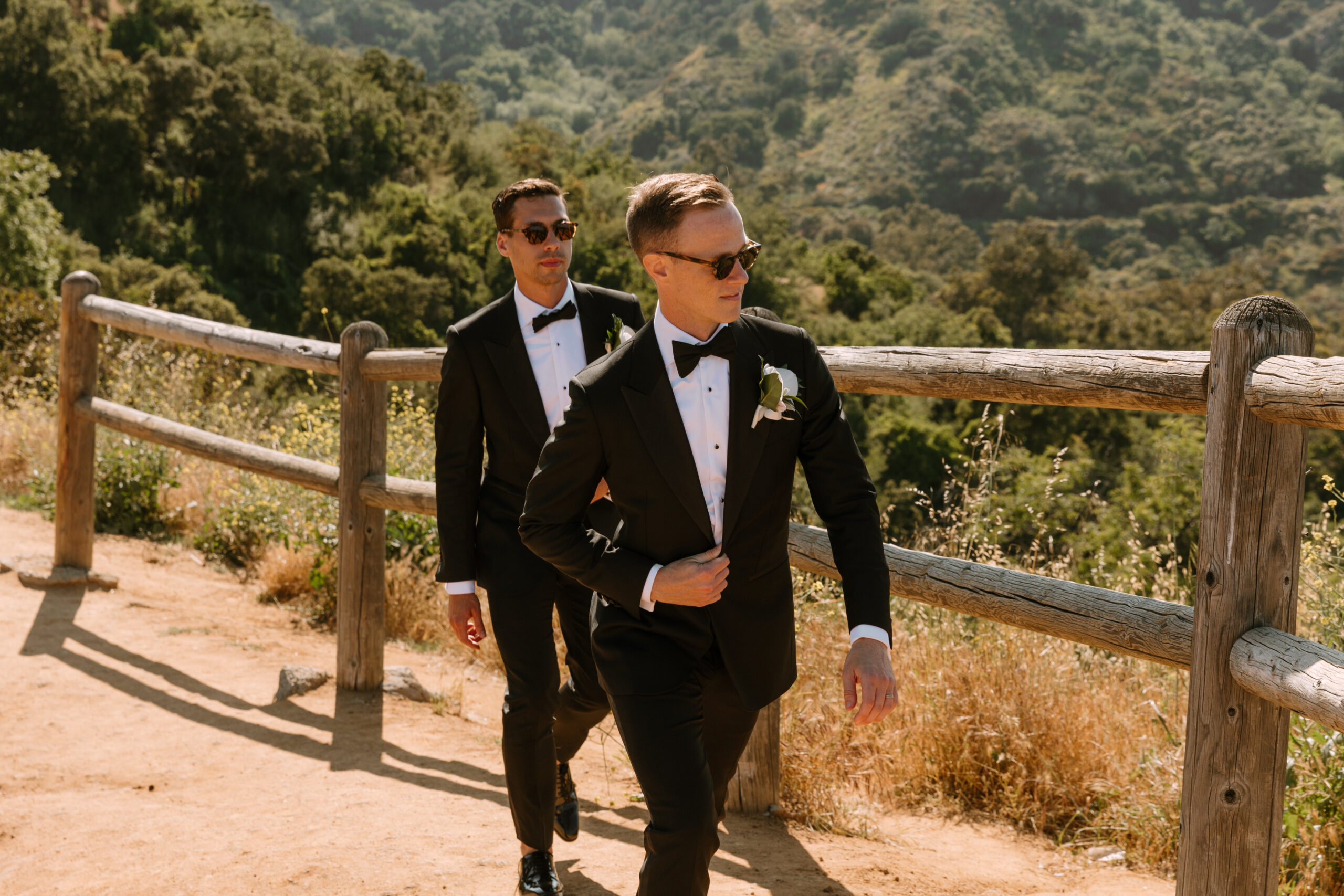 gay couple in tuxedos and sunglasses walks along railing near Mulholland Drive