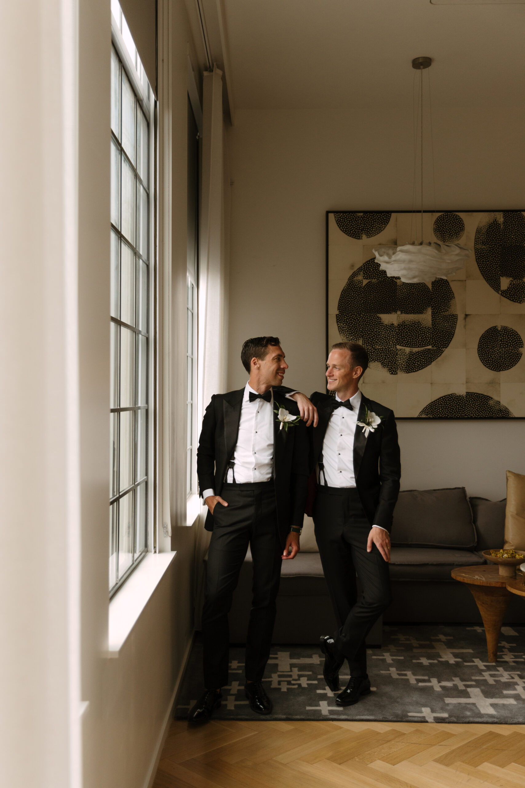 gay couple poses by window with arms around each other in Design Suite at Kimpton La Peer Hotel