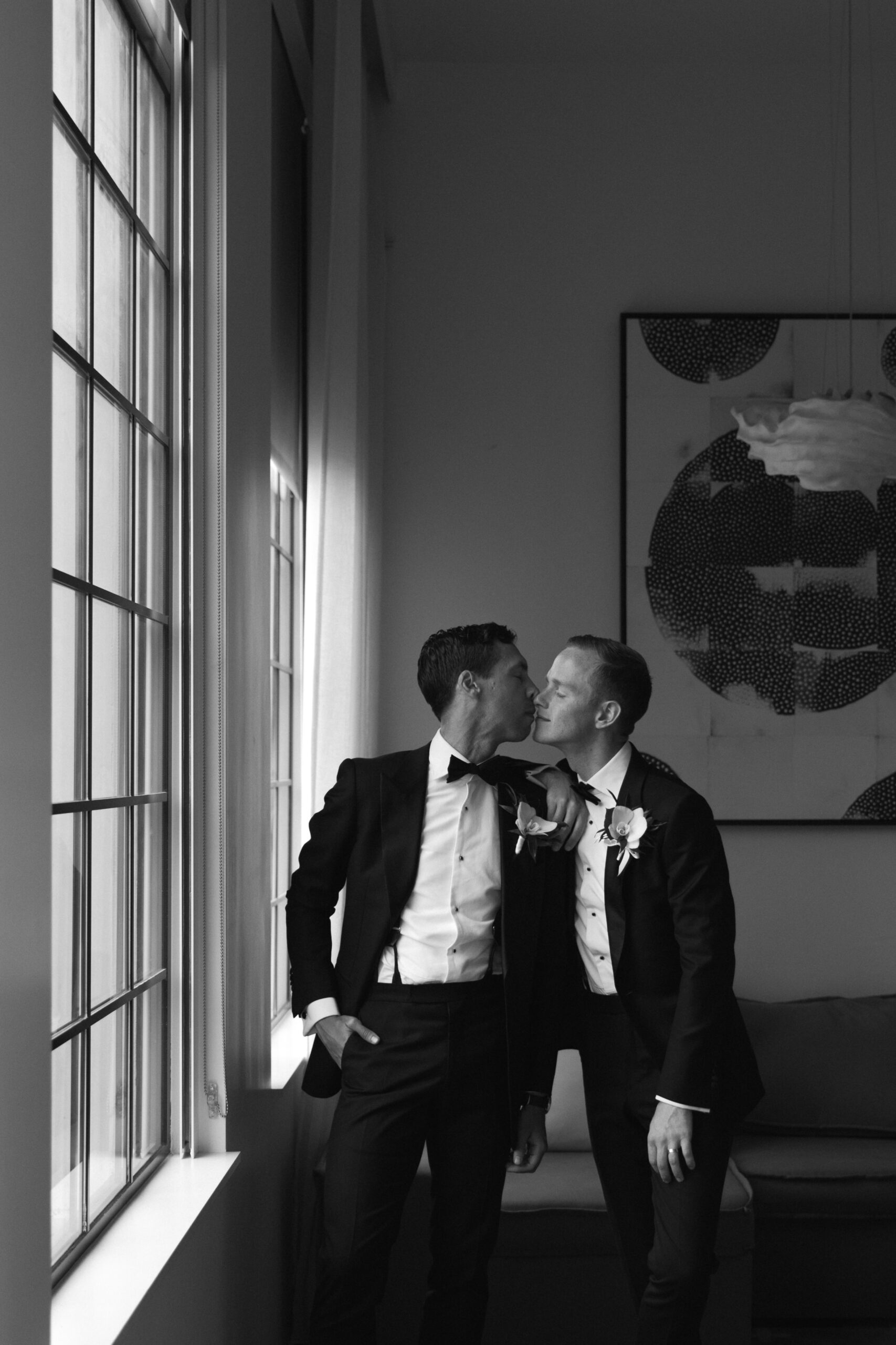 black and white photo of gay couple kissing by window with arms around each other in Design Suite at Kimpton La Peer Hotel