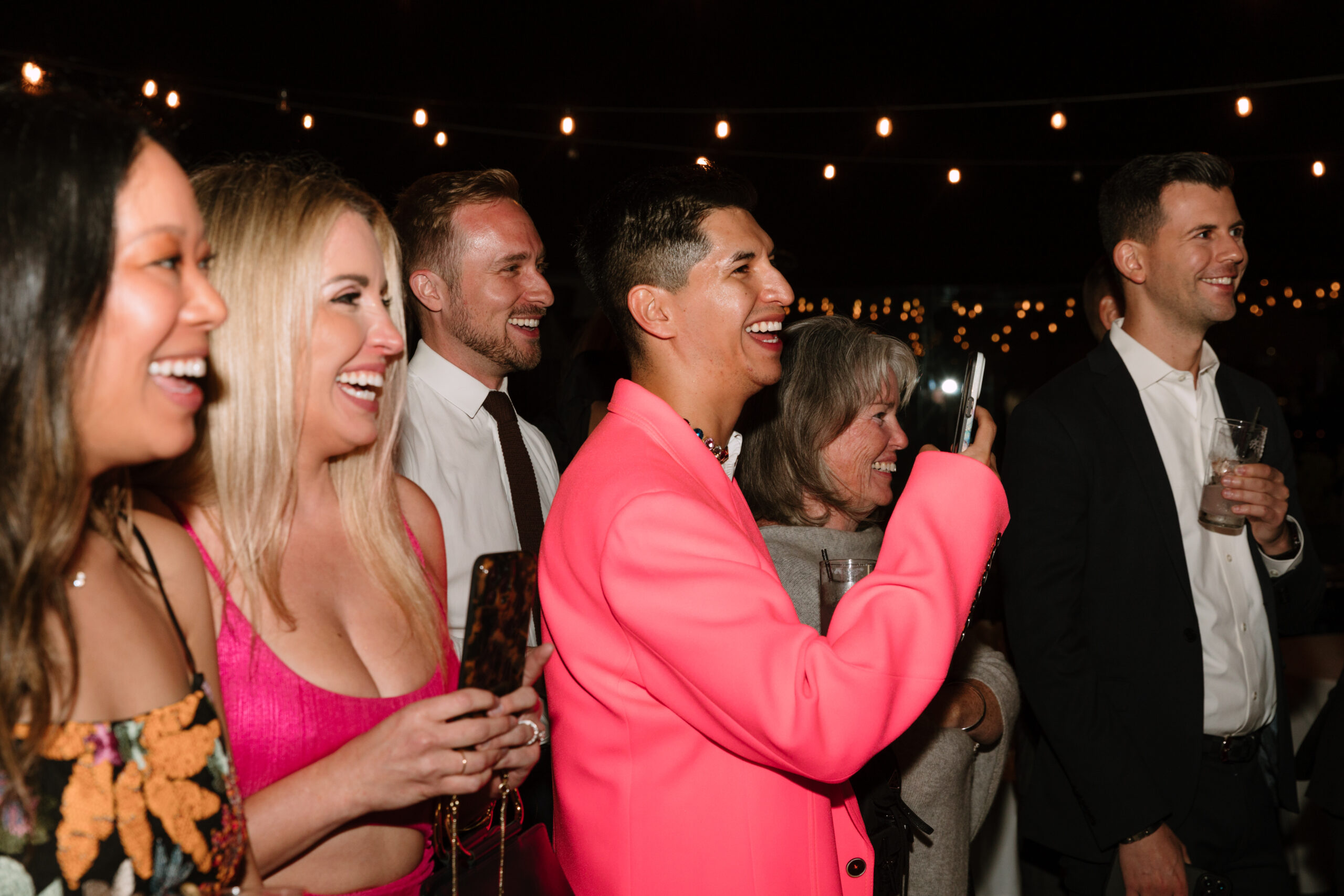 direct flash photo of guests in bright pink smiling and taking pictures on their phones