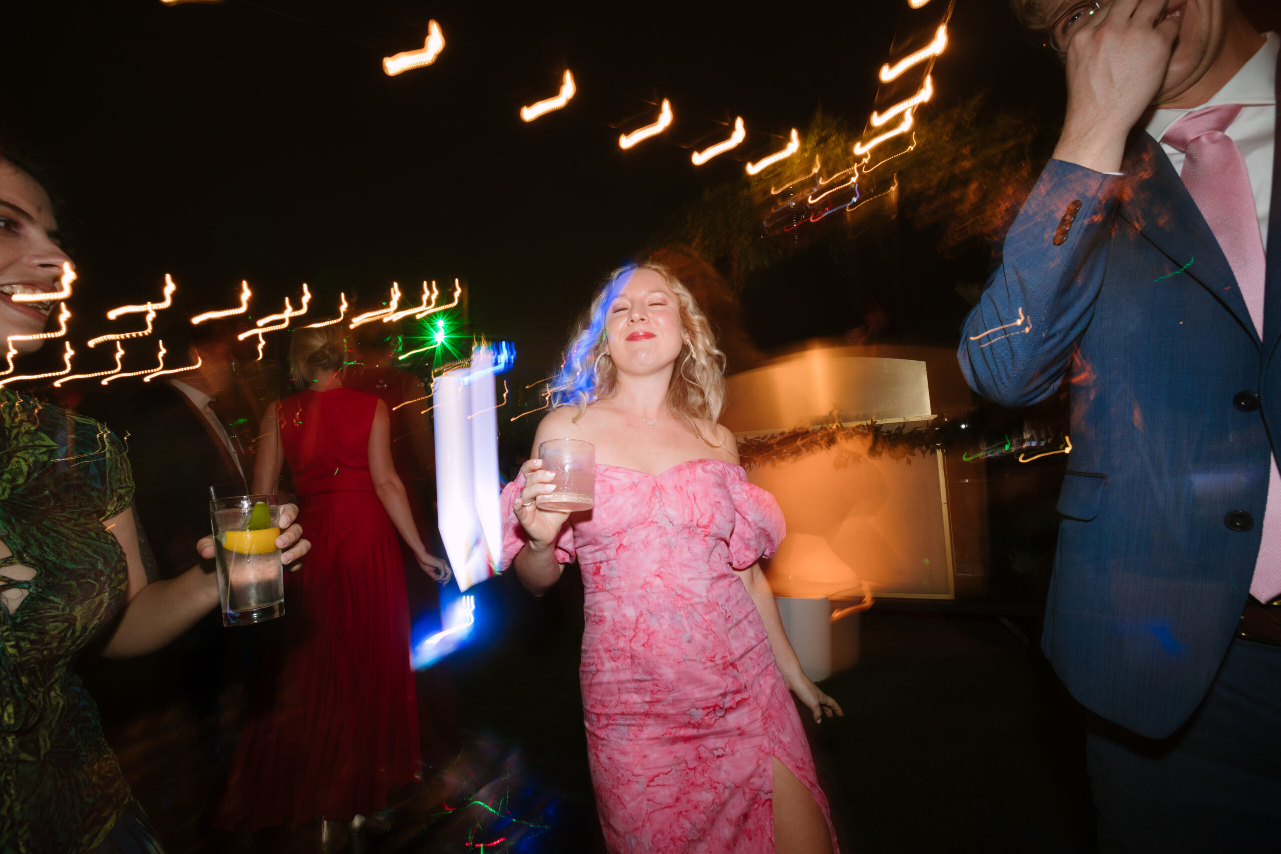 shutter drag flash photo of wedding guest in pink dress dancing with a cocktail