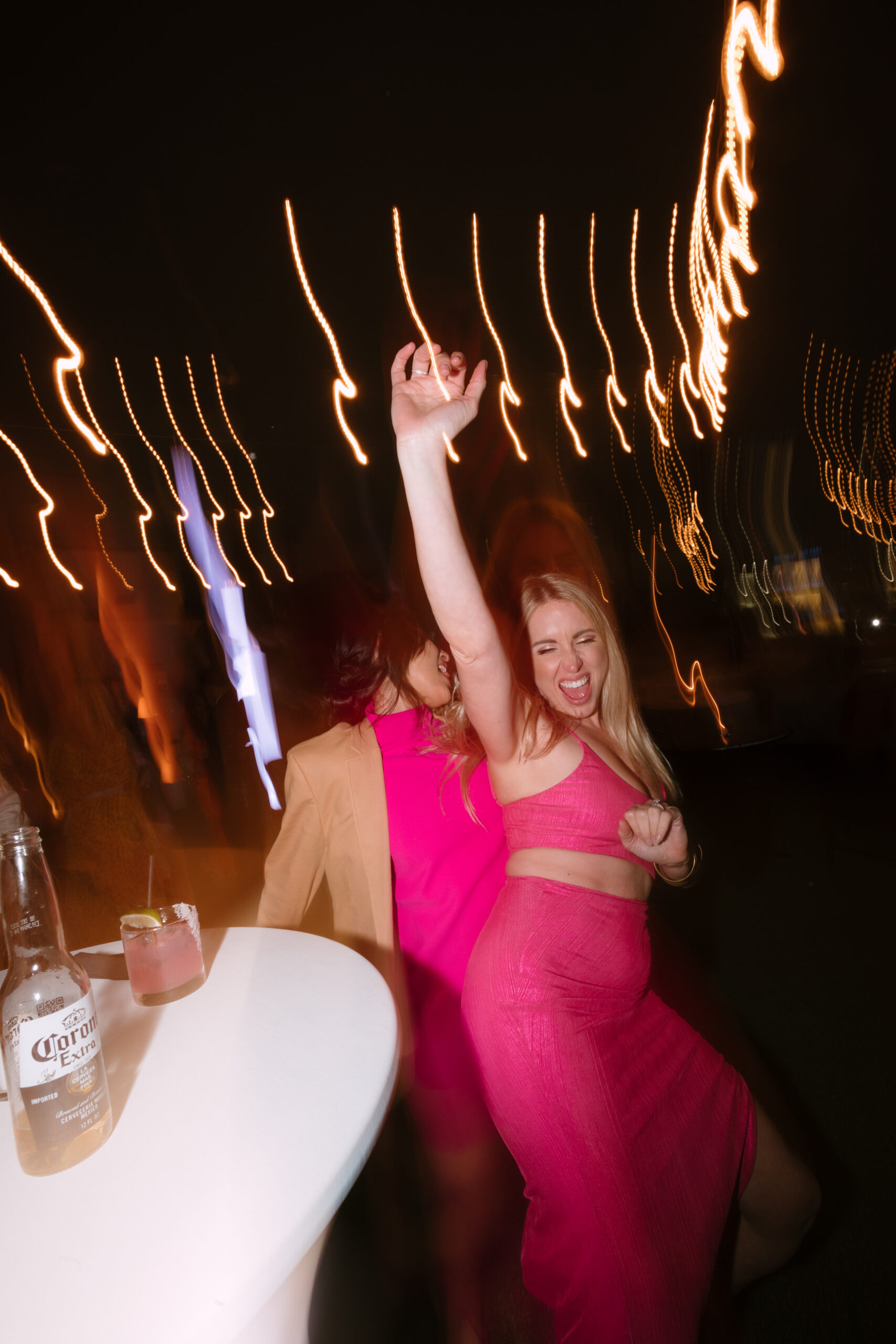 shutter drag flash photo of wedding guests in hot pink dancing with their hands in the air
