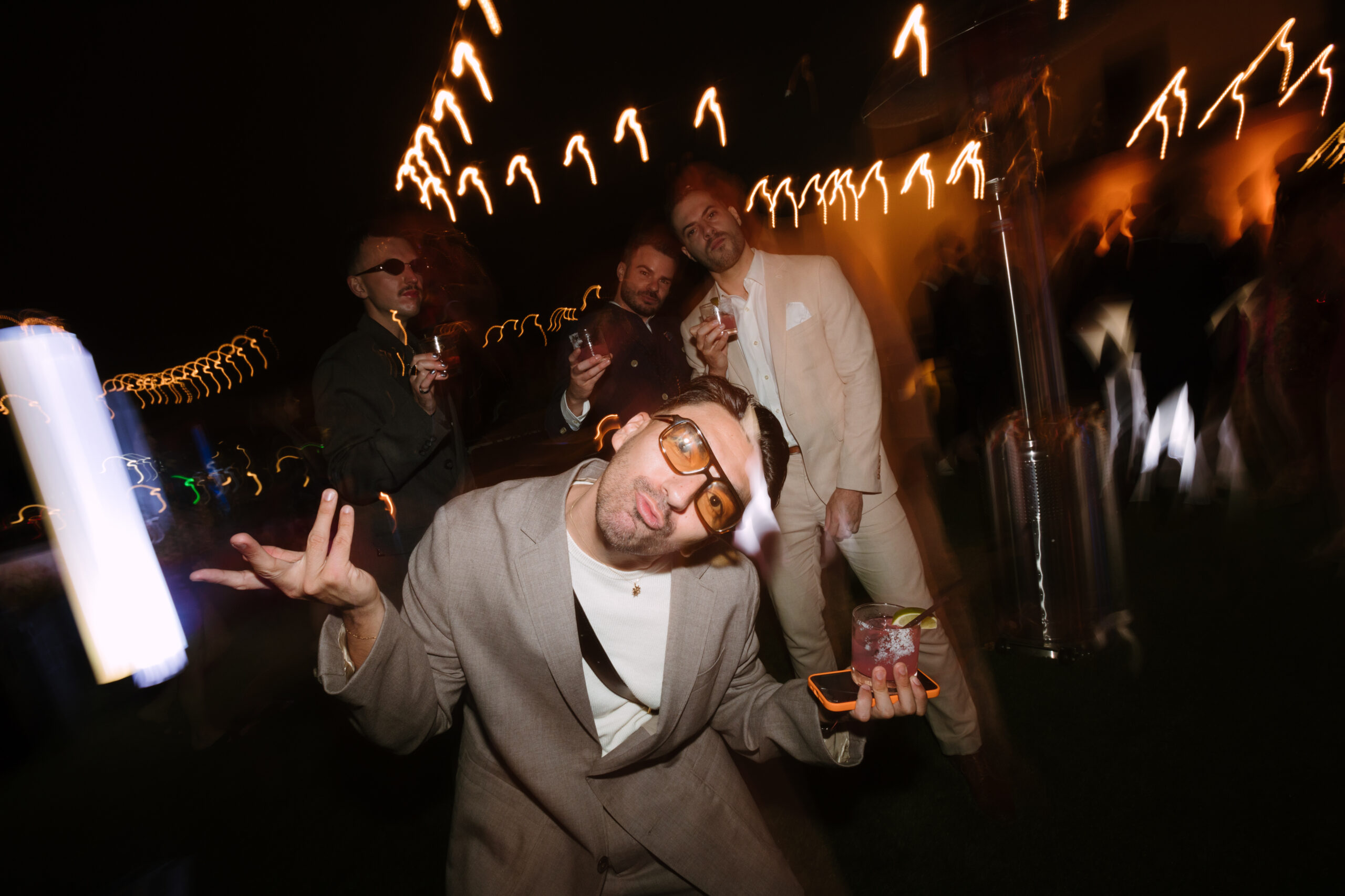 shutter drag flash photo of wedding guest dancing with a cocktail and phone in his hand