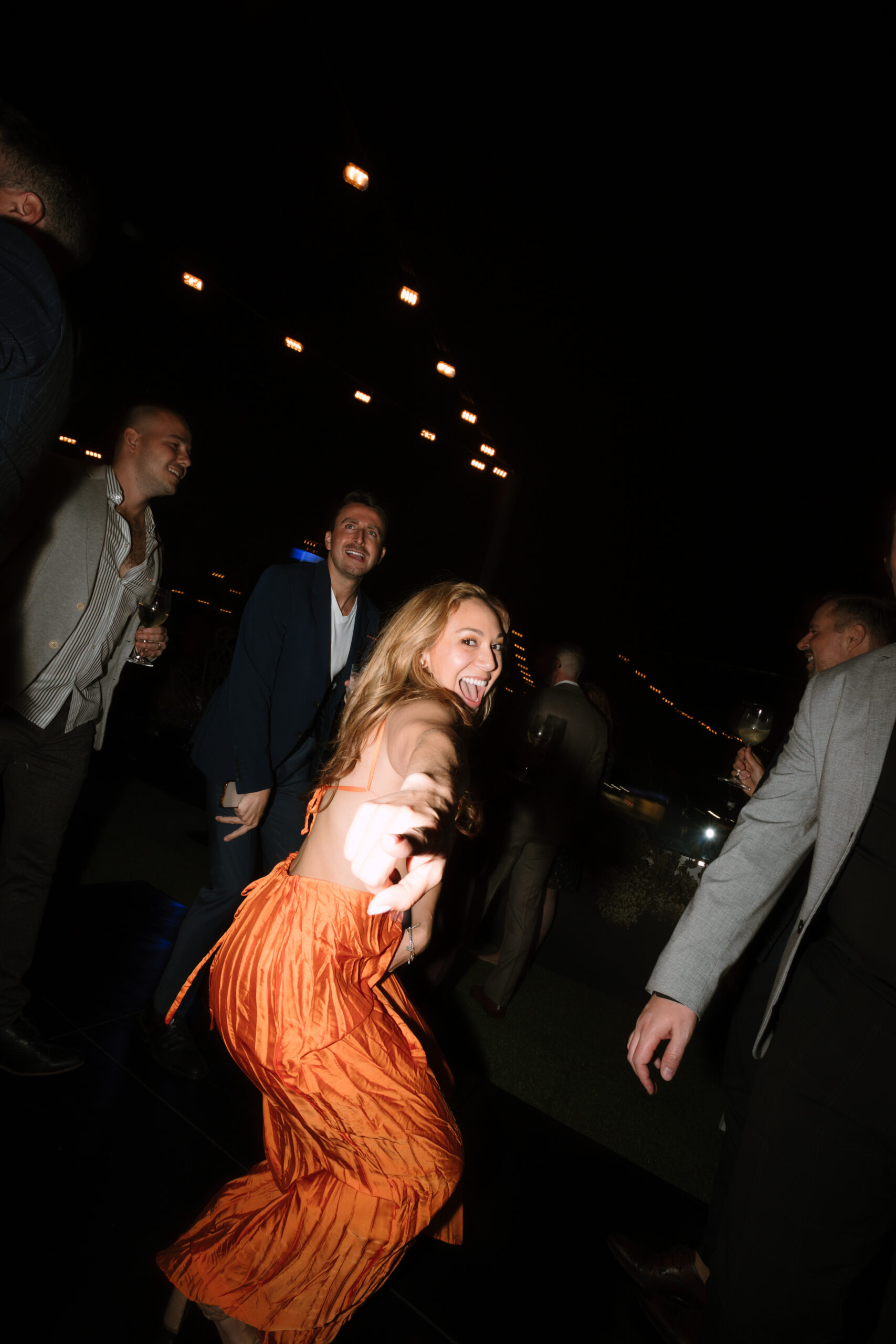 direct flash photo of wedding guest in orange dress dancing and pointing at the camera