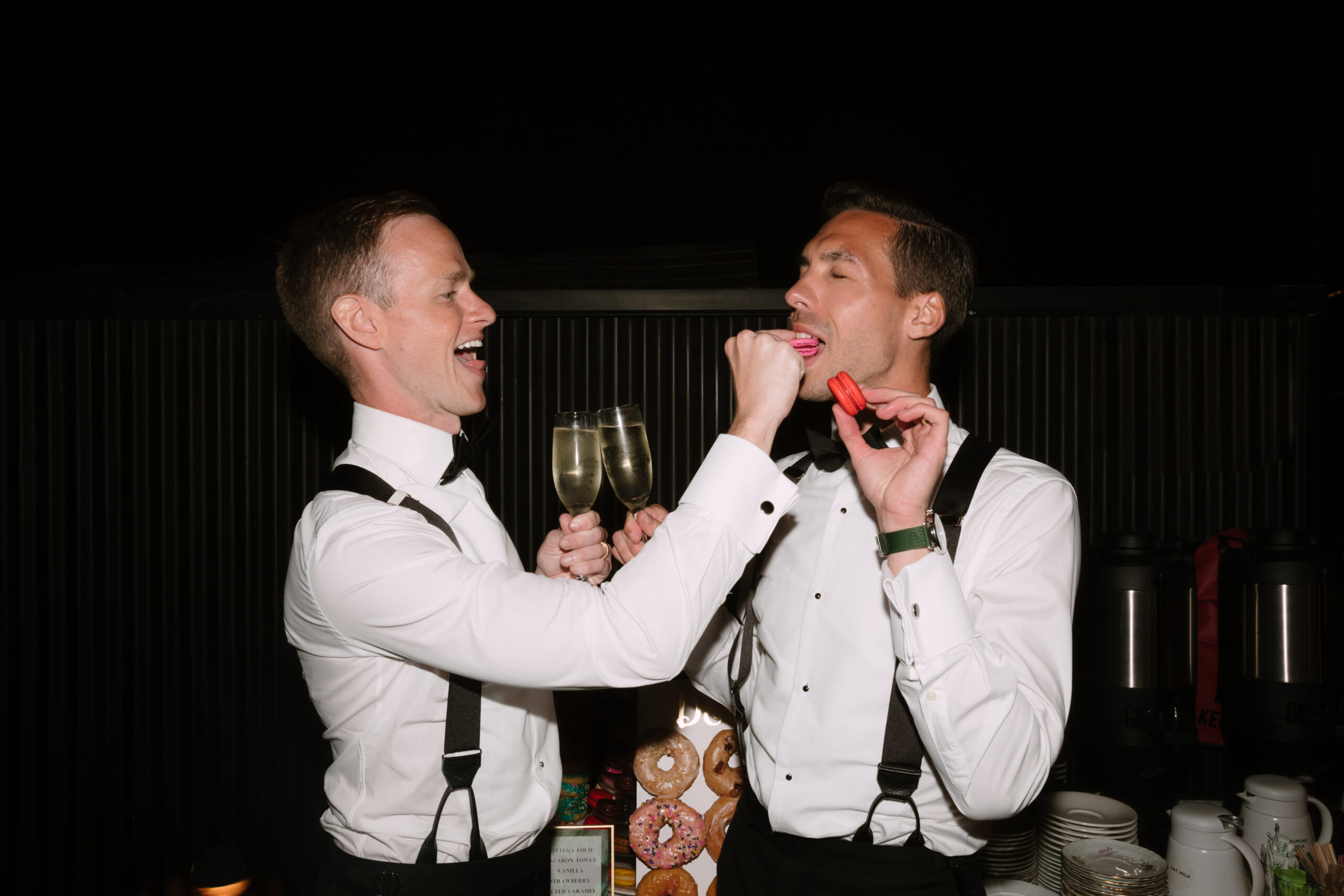 direct flash photo of gay grooms sharing colorful macarons with each other