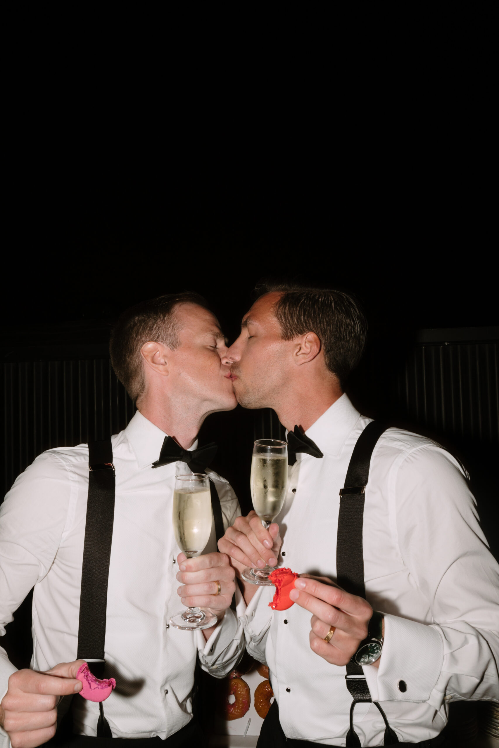 direct flash photo of gay grooms kissing while toasting with champagne flutes
