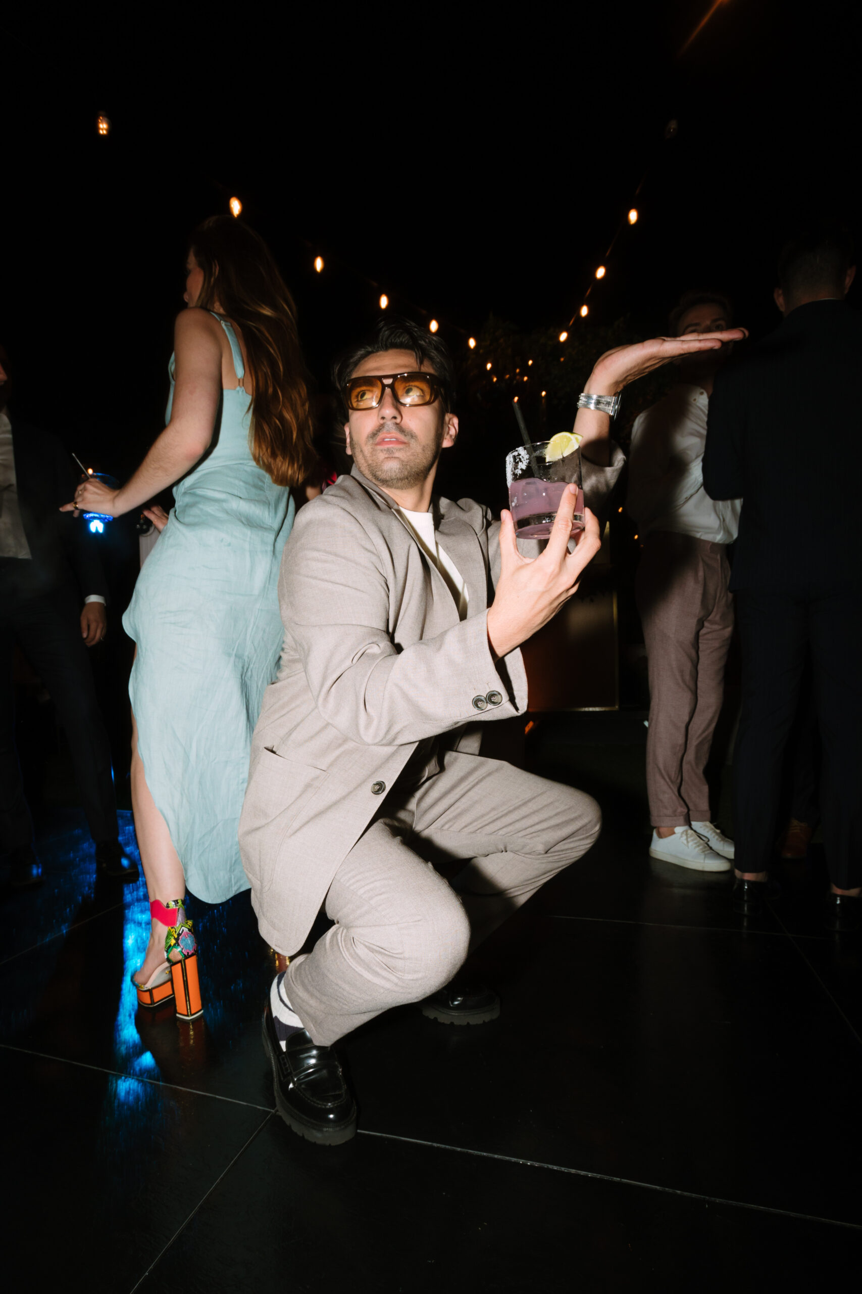 direct flash photo of wedding guest duckwalking on the dance floor with a cocktail in his hand