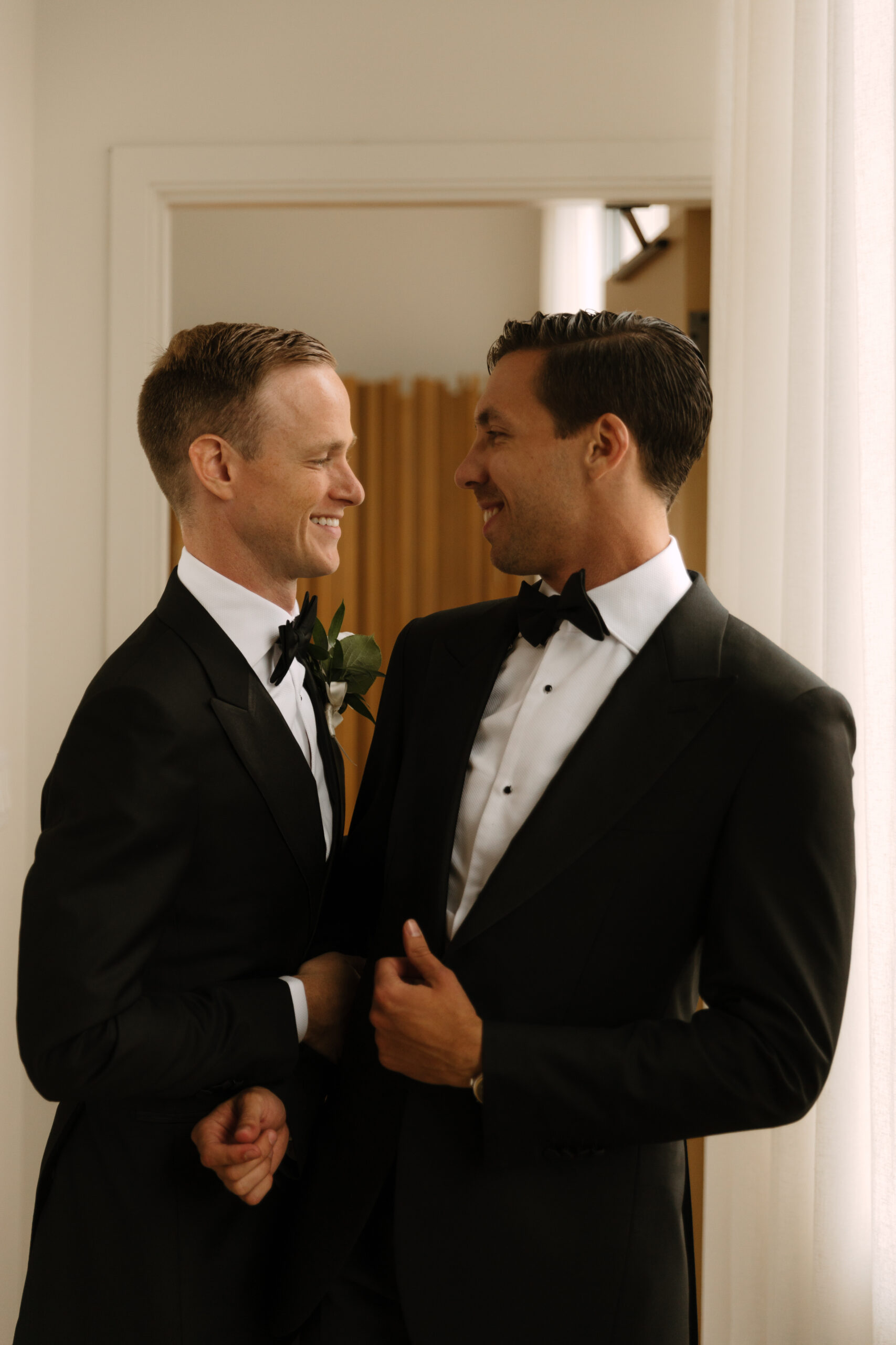 gay couple looks fondly at each other after getting dressed for their wedding