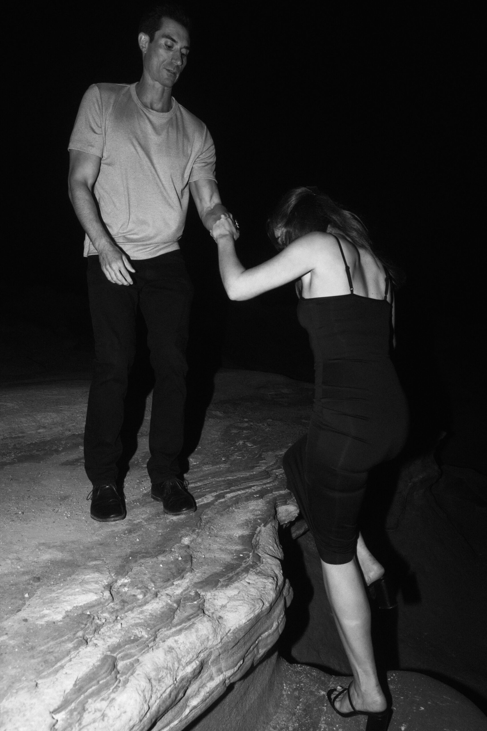 black and white flash photo of groom helping bride up Sunset Cliffs 