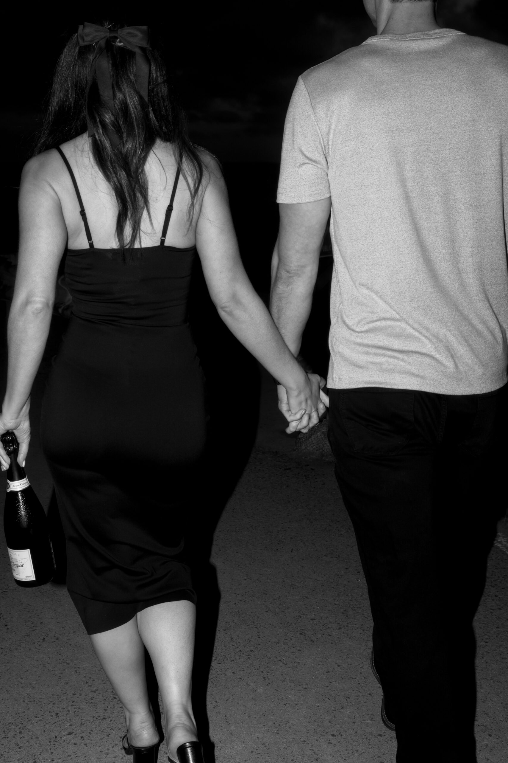 black and white direct flash photo of couple holding hands with a bottle of champagne