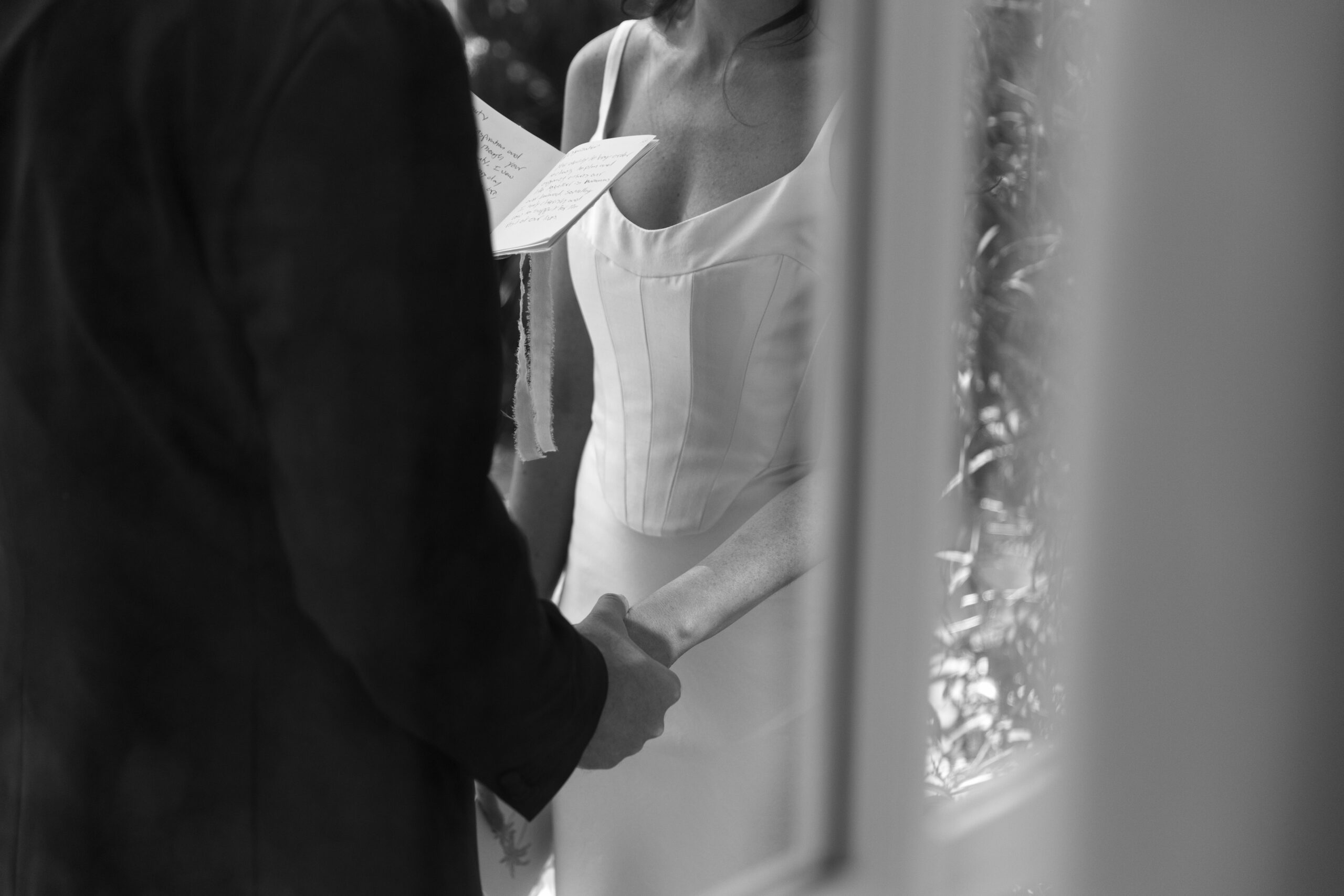 black and white crop of bride and groom holding hands through a window