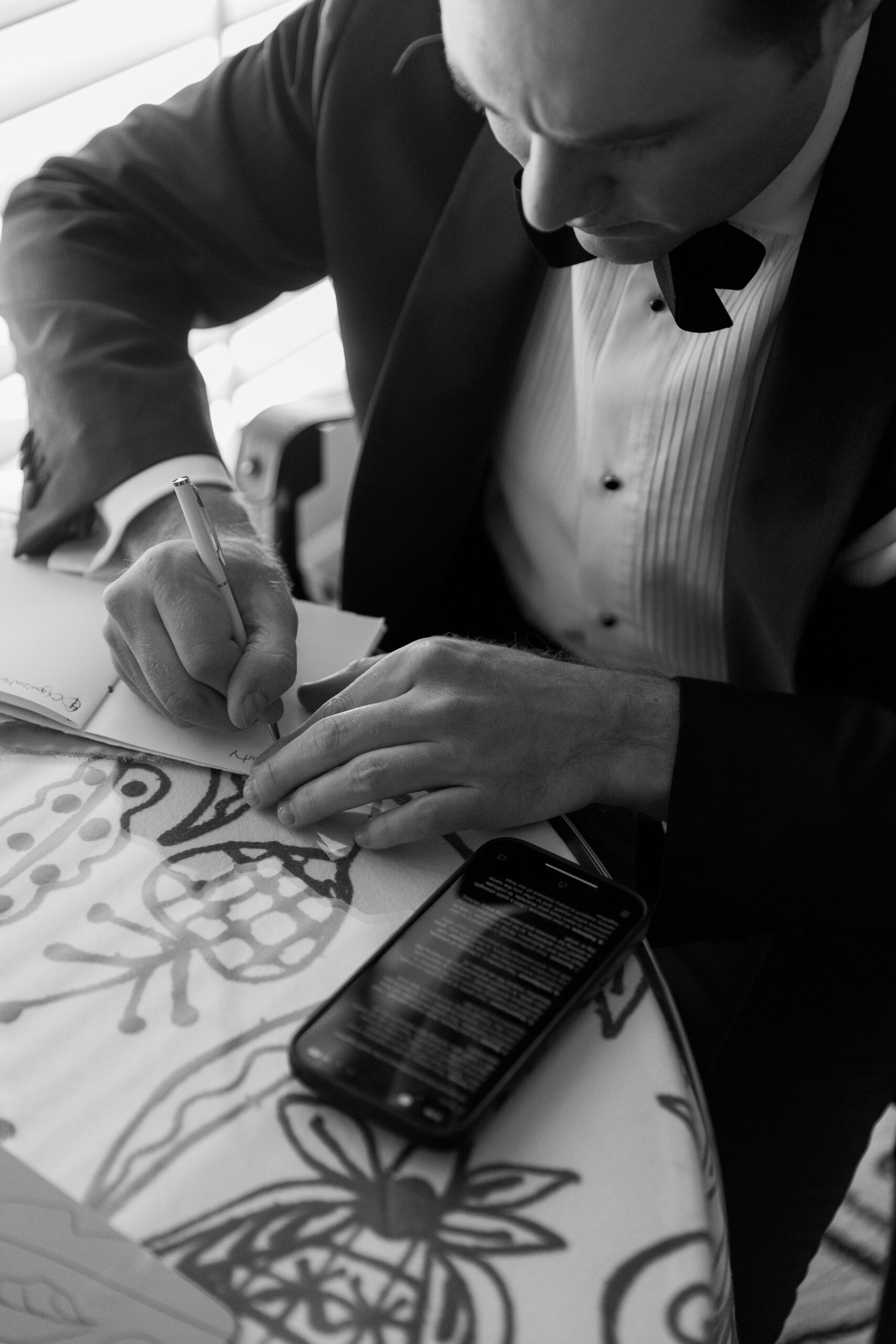 black and white photo of groom copying his vows into a vow book