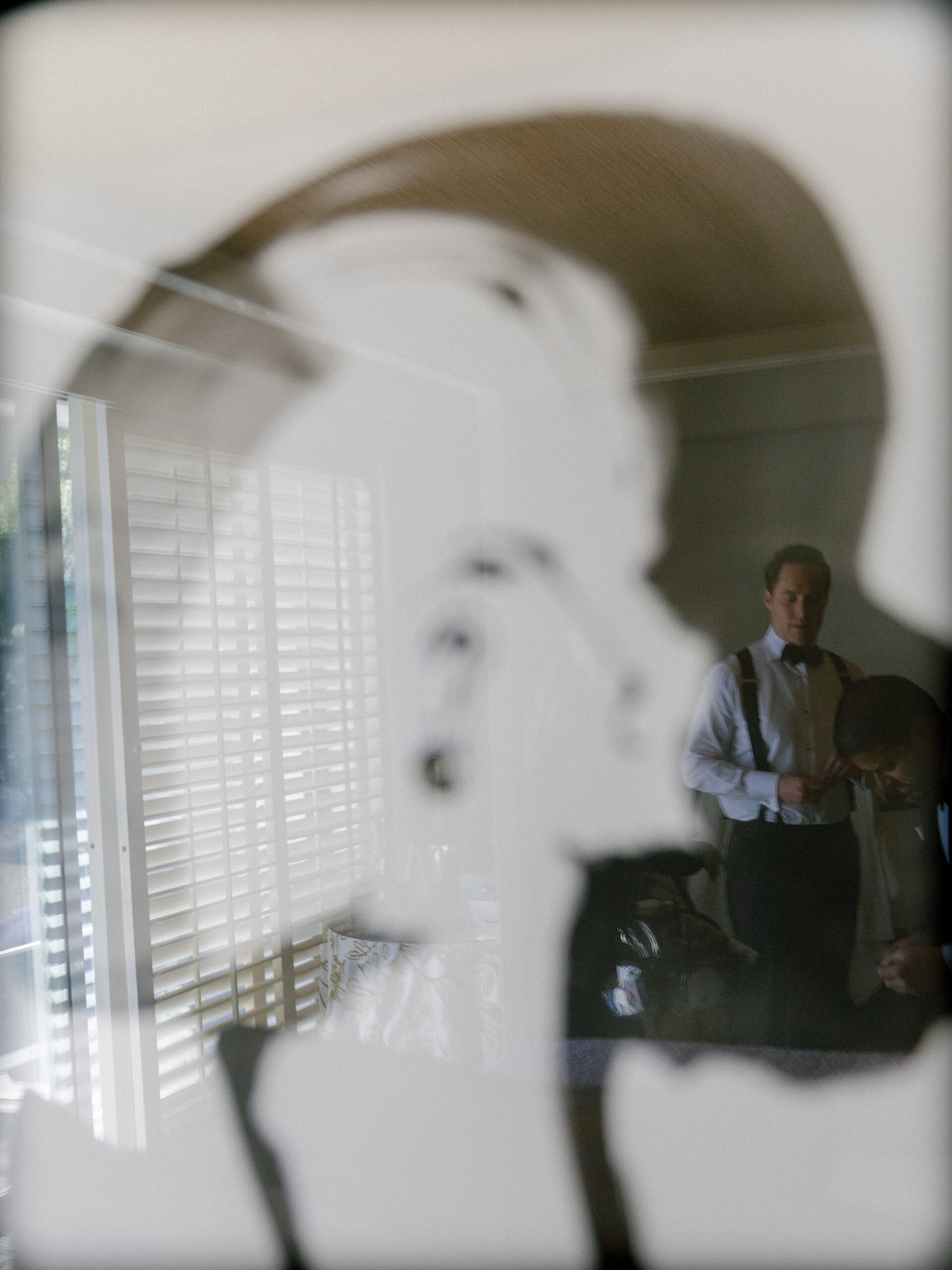 film photo of groom reflected in glass of framed art while he's getting ready