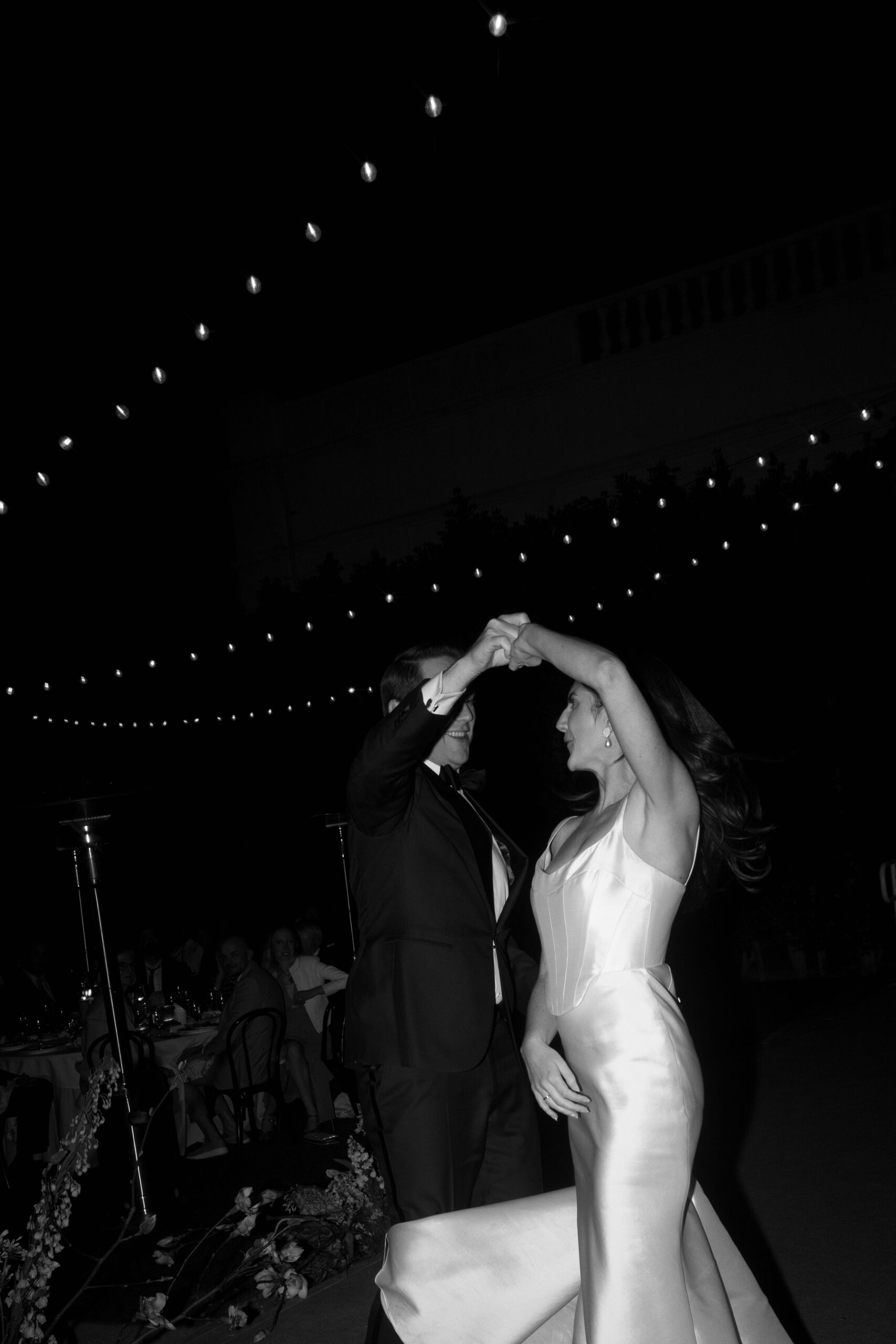 flash photo of groom twirling bride under cafe lights on banquet lawn