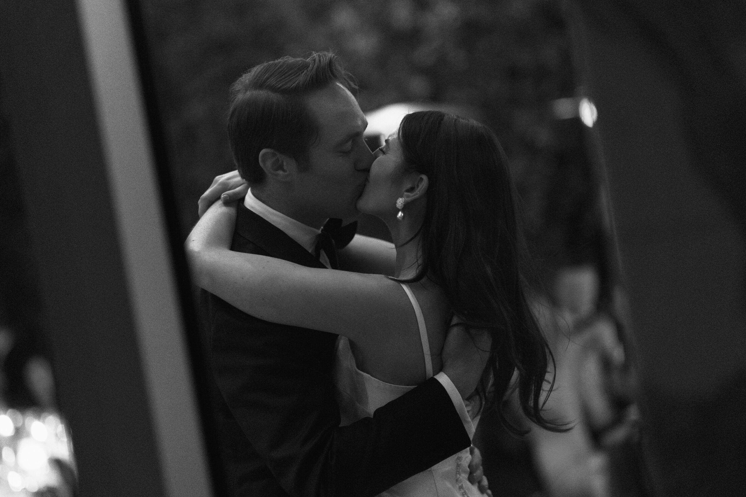 black and white grainy photo shot through window of bride and groom kissing after first dance