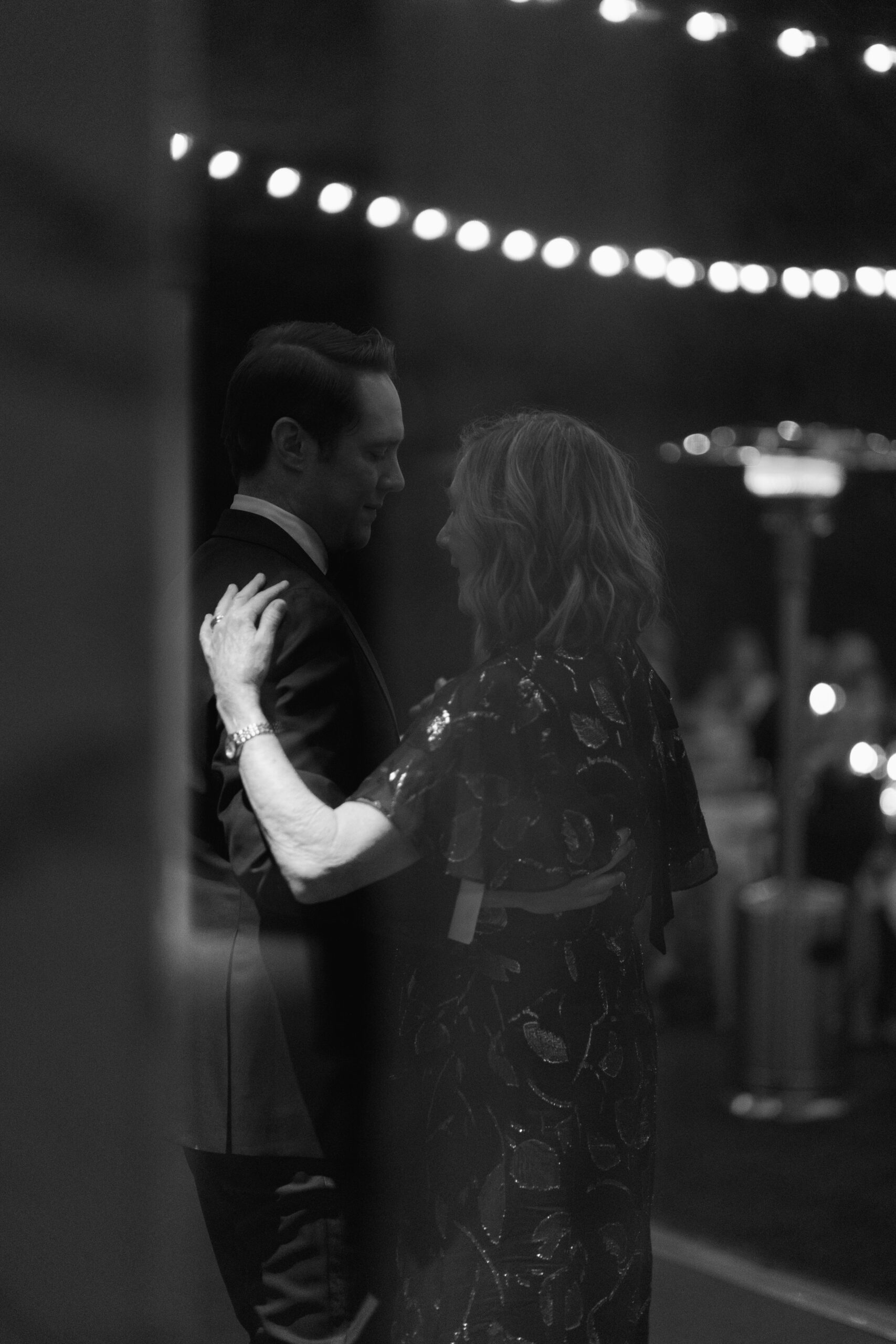 black and white photo through window of groom and mother having first dance