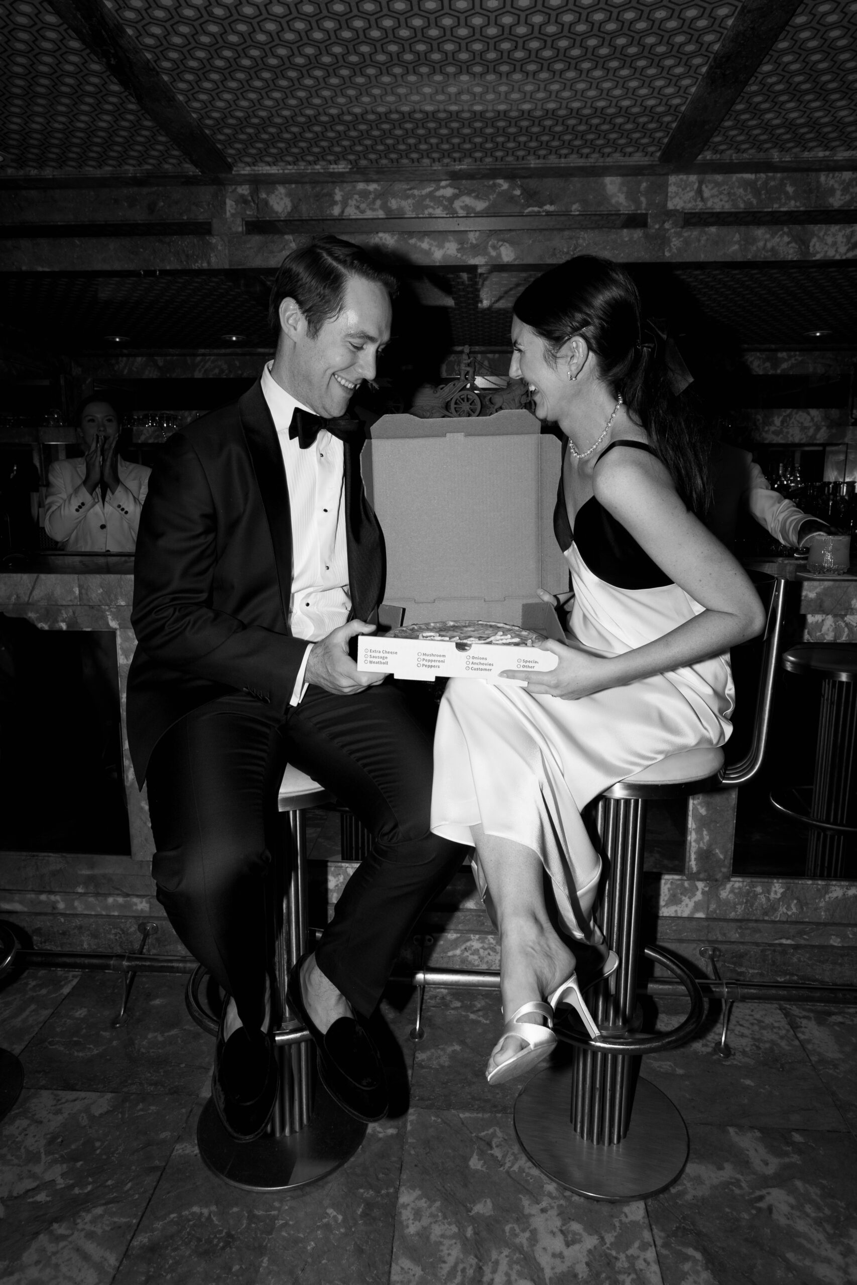 black and white flash photo of bride and groom sitting in parker mini bar sharing just married pizza