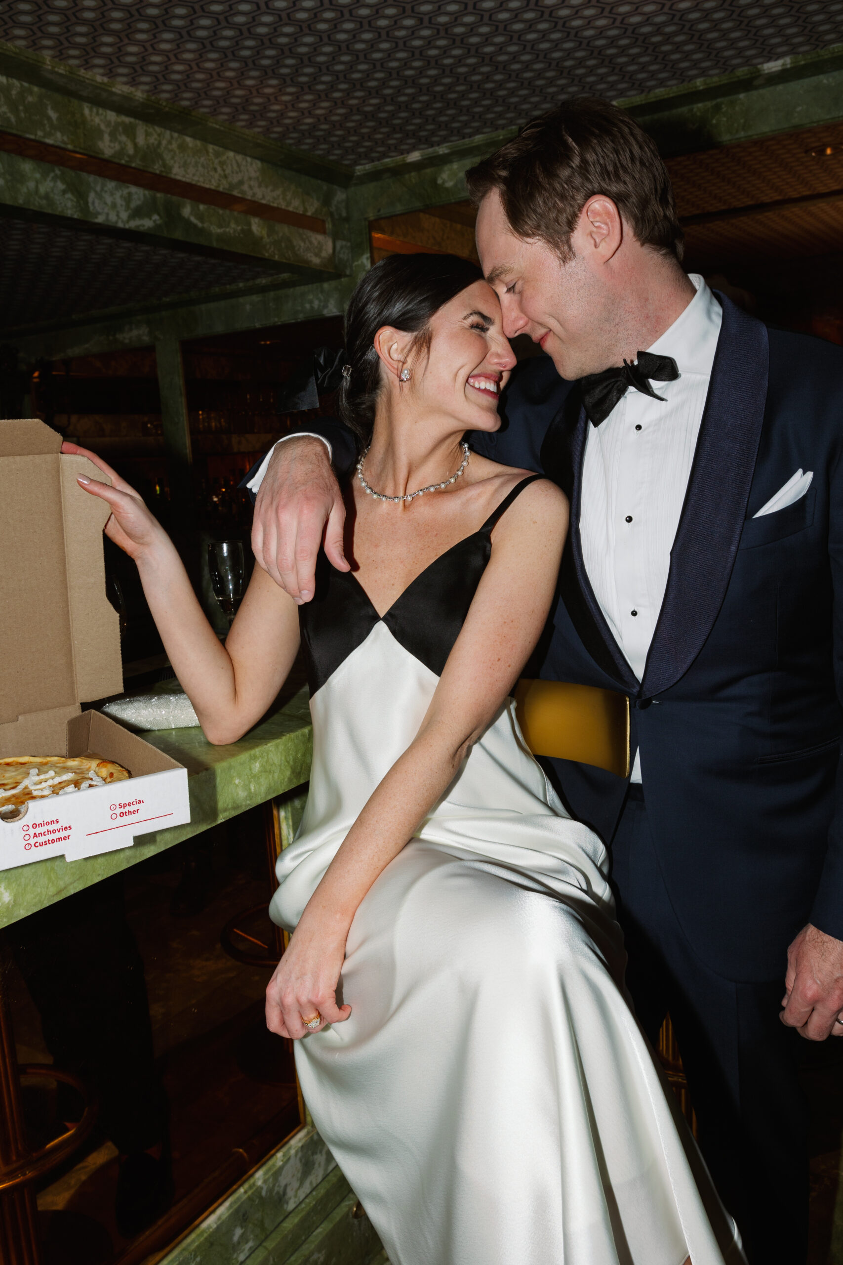 flash photo of bride and groom cuddling in mini bar with just married pizza