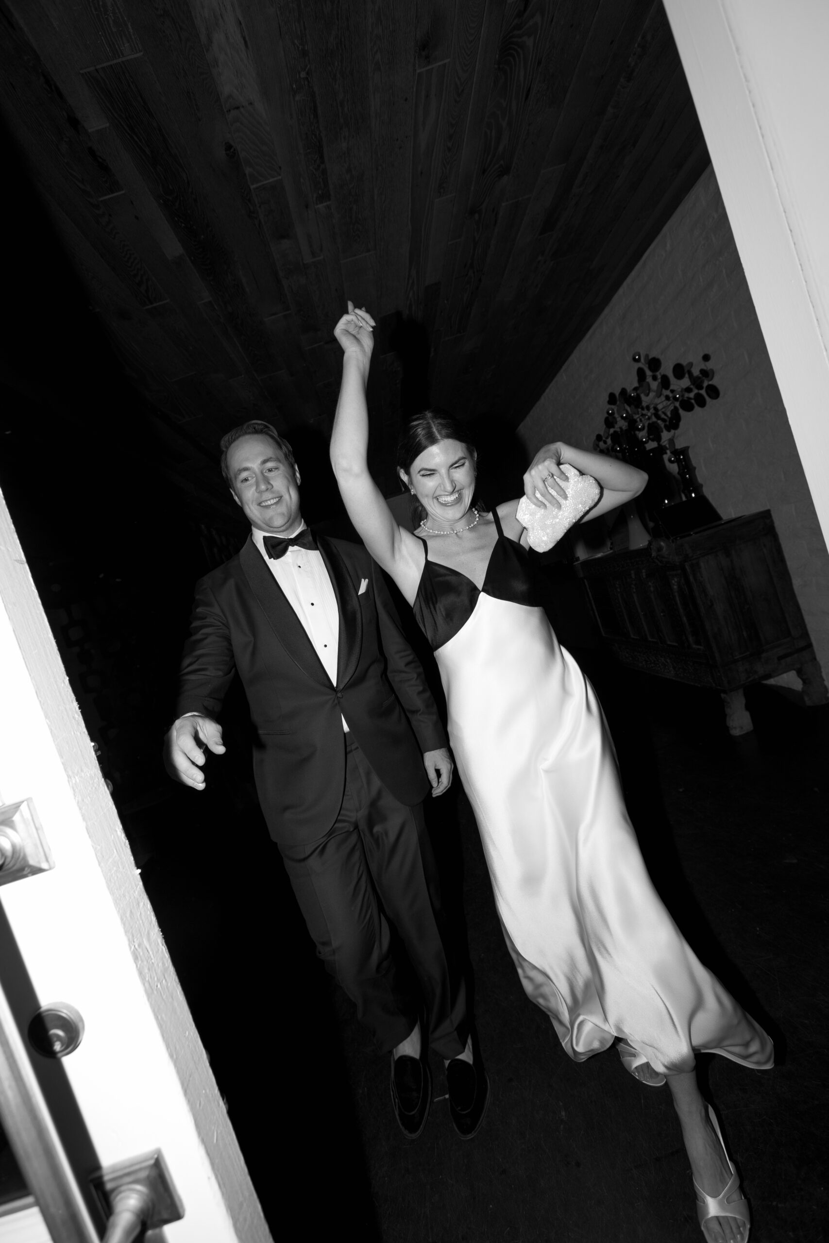 black and white flash photo of bride and groom in outfit change walking through open door back to reception