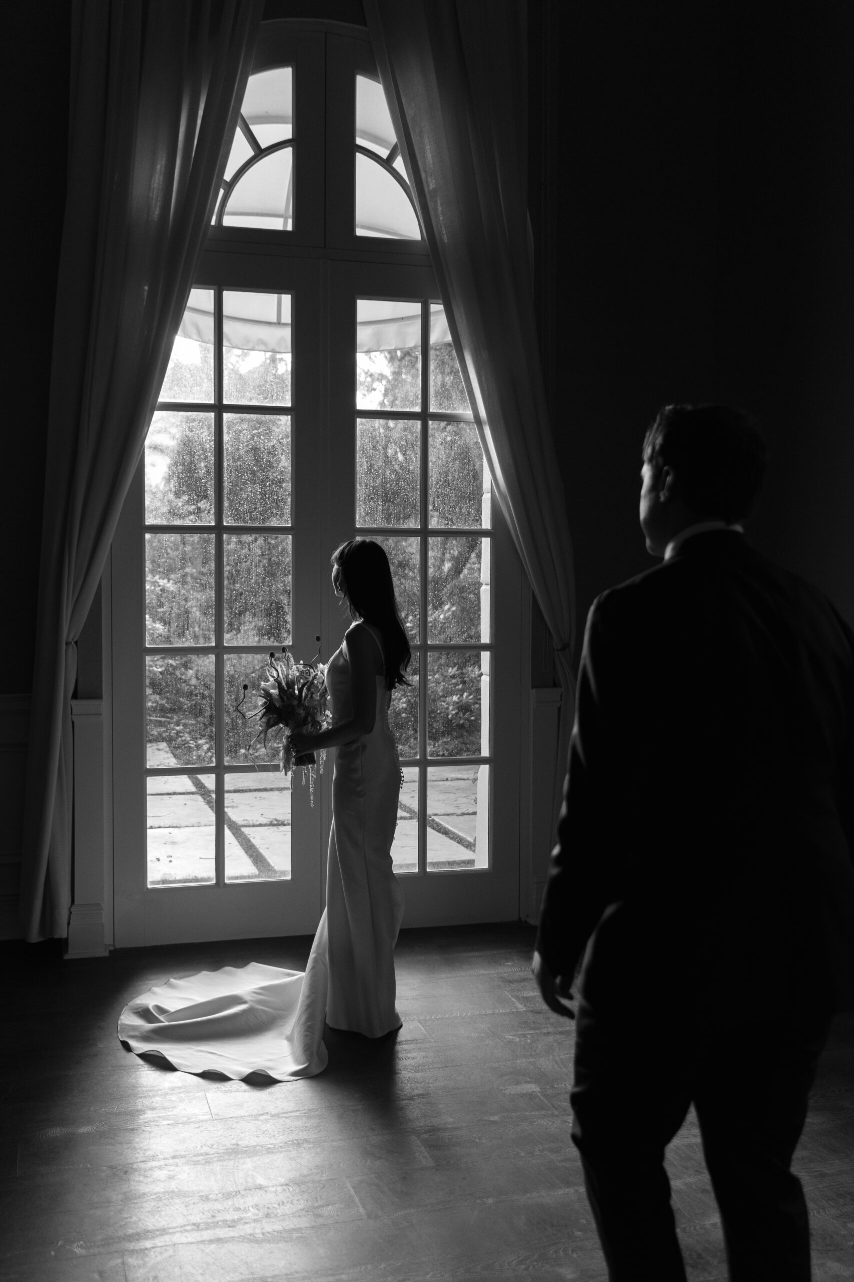 black and white of groom walking up behind bride standing in front of window in Mafia Suite of Parker Palm Springs