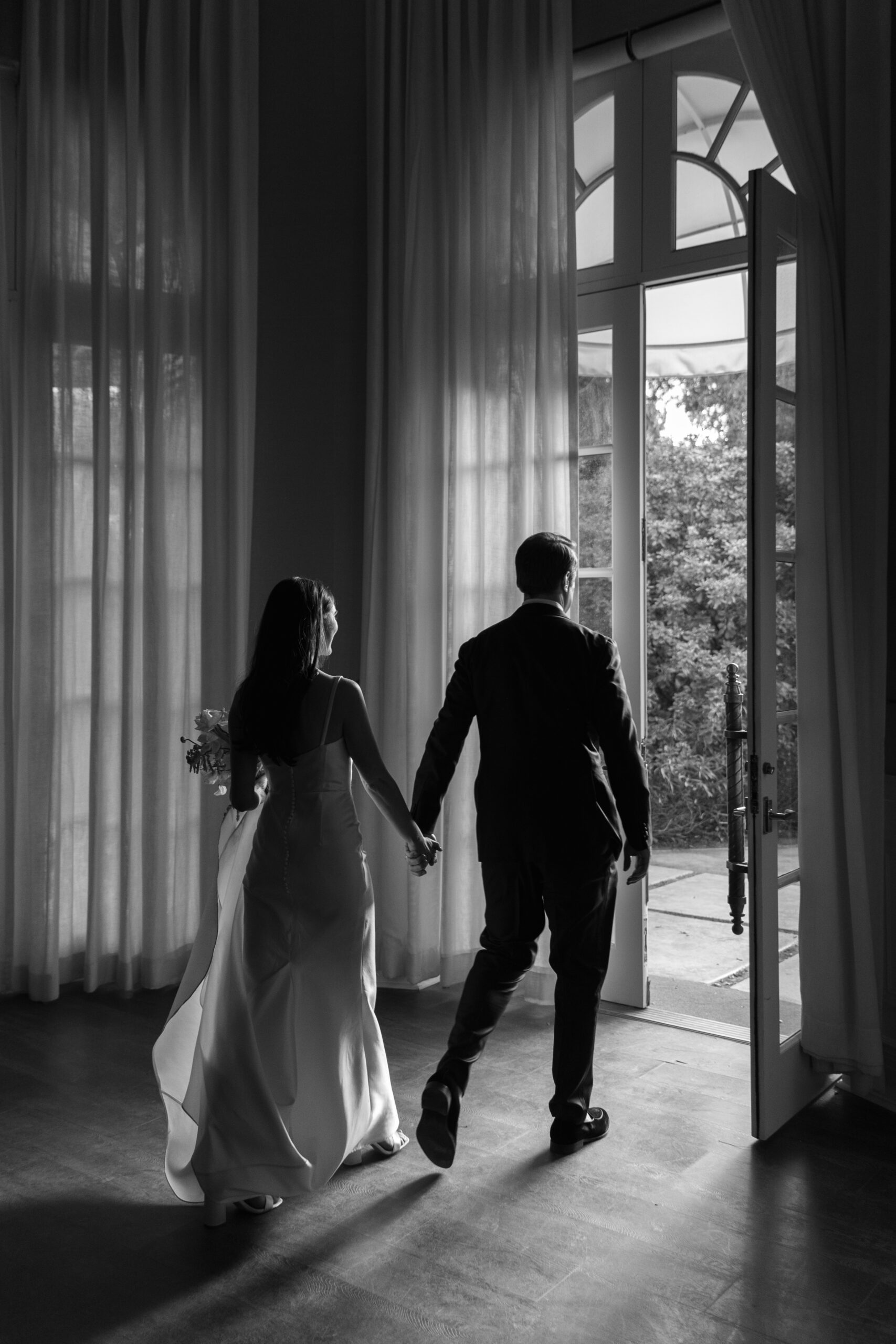 black and white from behind of bride and groom holding hands exiting the Mafia Suite at Parker palm springs