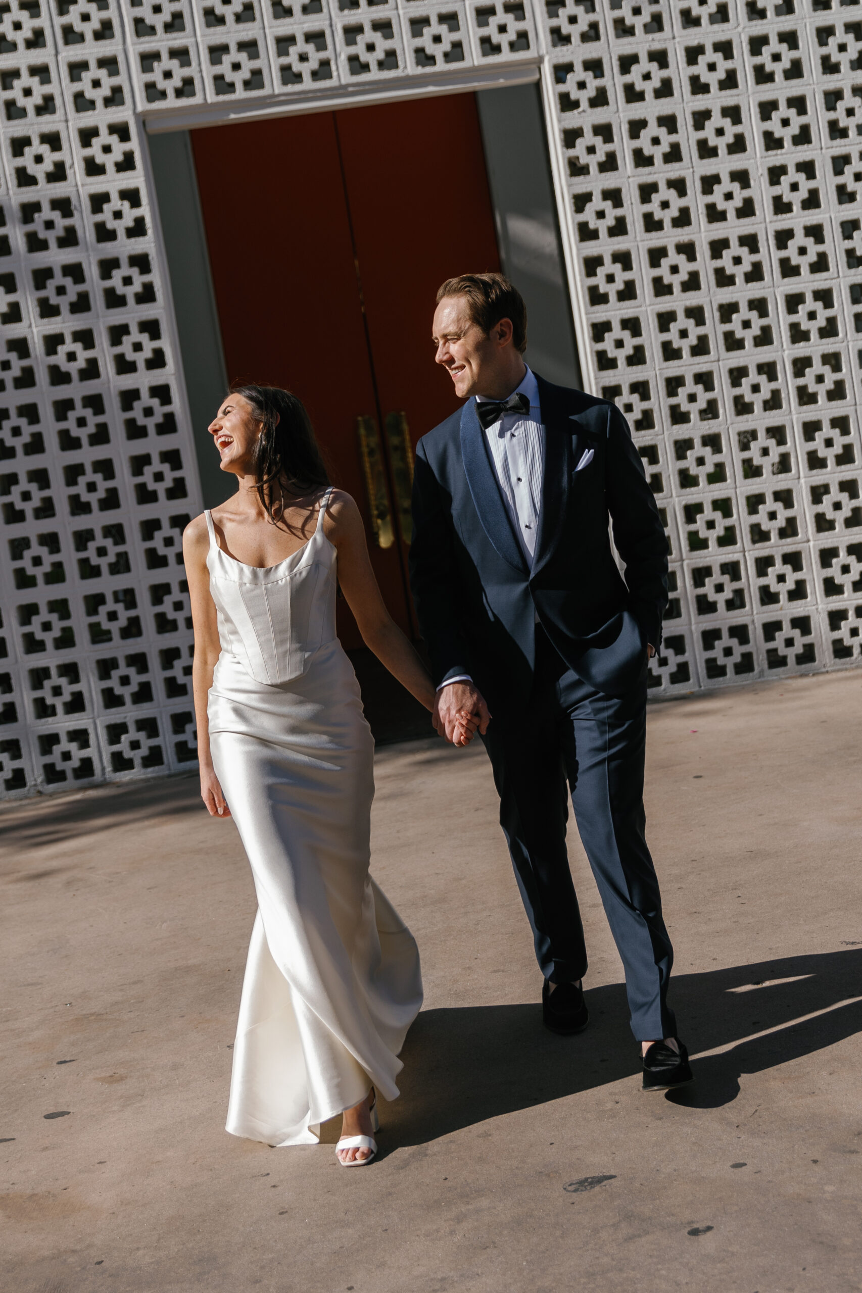 bride and groom walking and laughing toward camera from entrance of Parker Palm Springs