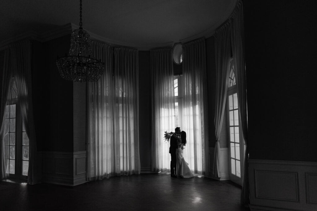 black and white wide shot in Mafia Suite of parker Palm springs of couple embracing by windows