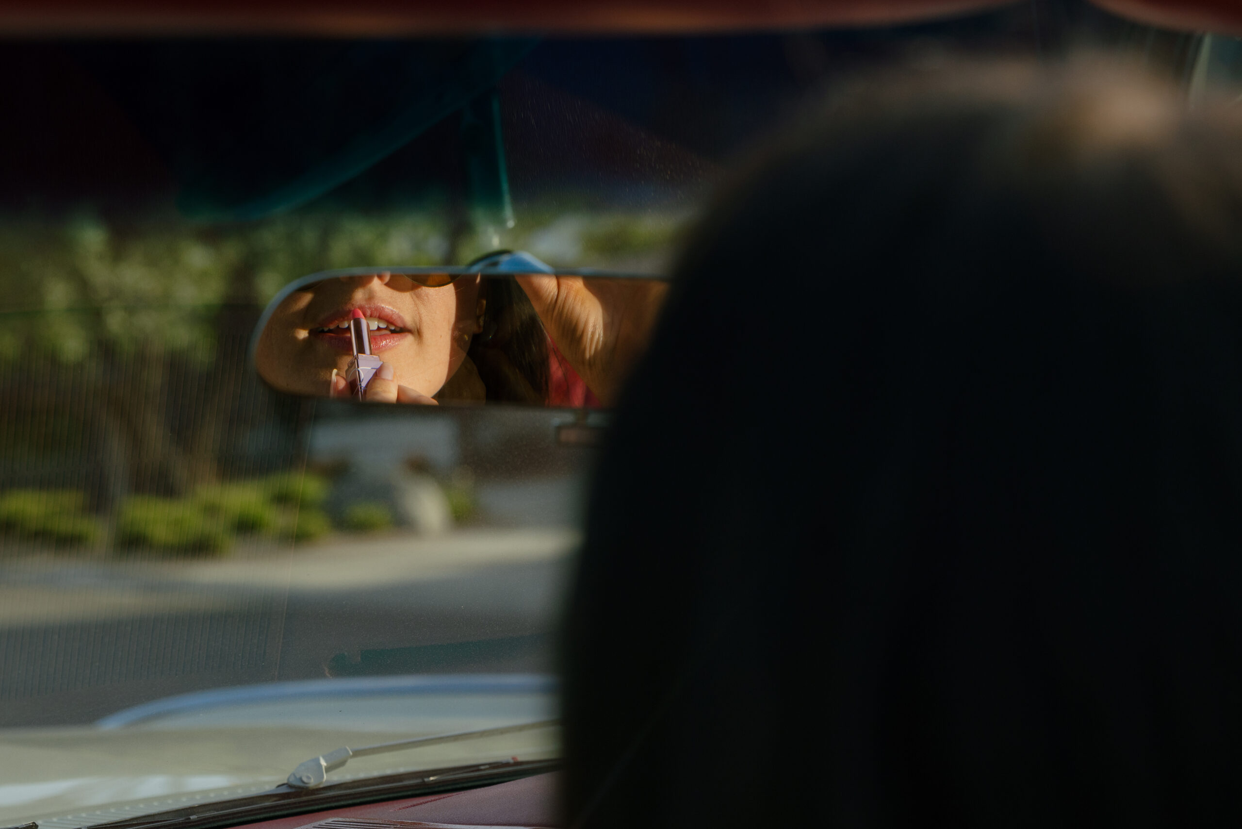 girl retouching lipstick in rearview mirror