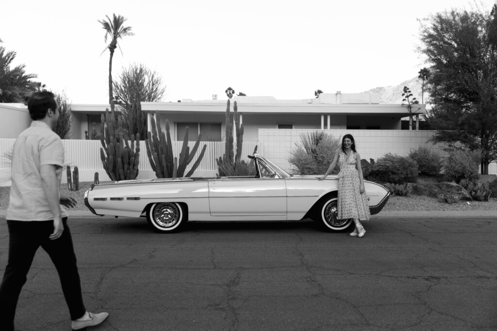 groom walking toward bride standing outside parked vintage convertible in front of Palm Springs house