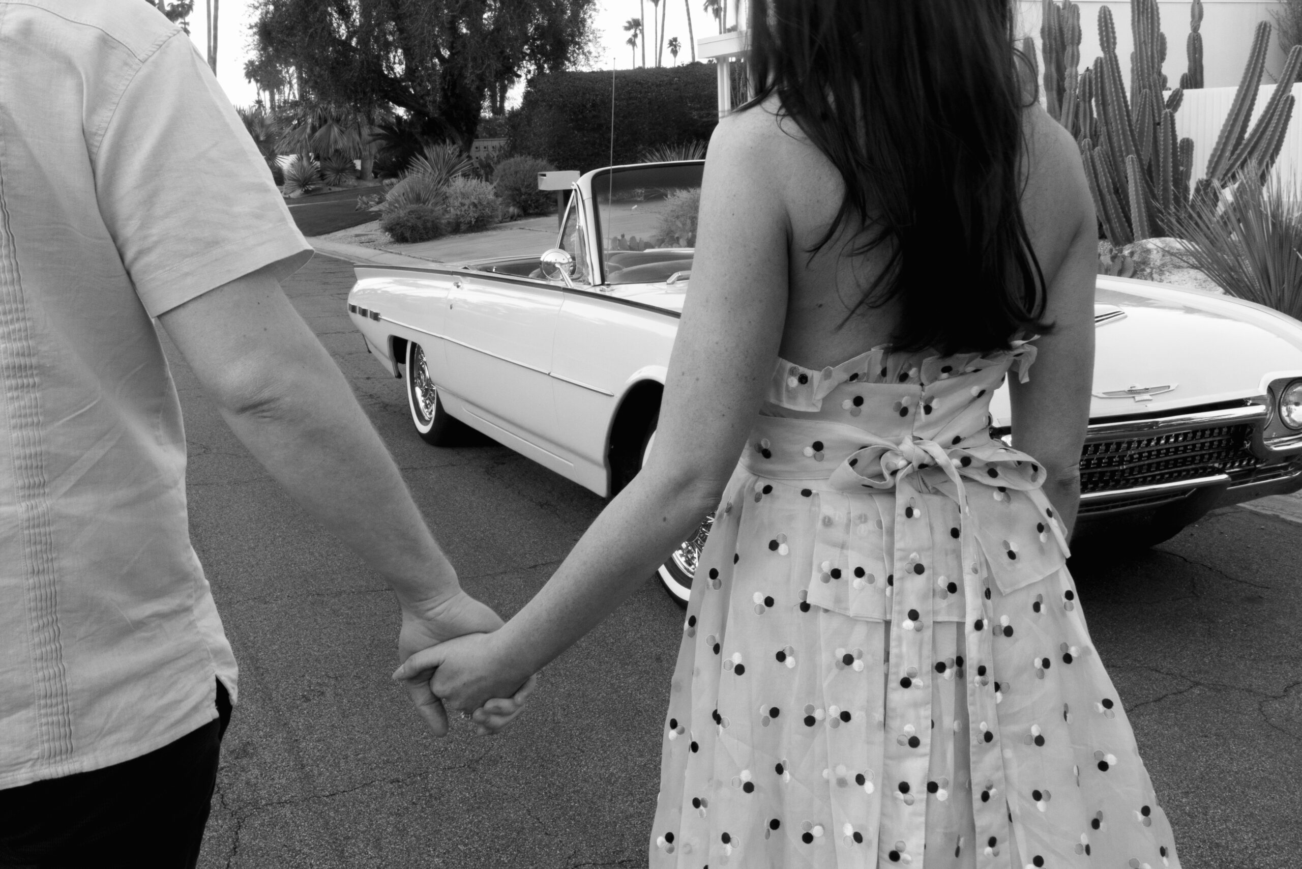 black and white close up of couple holding hands in front of vintage convertible