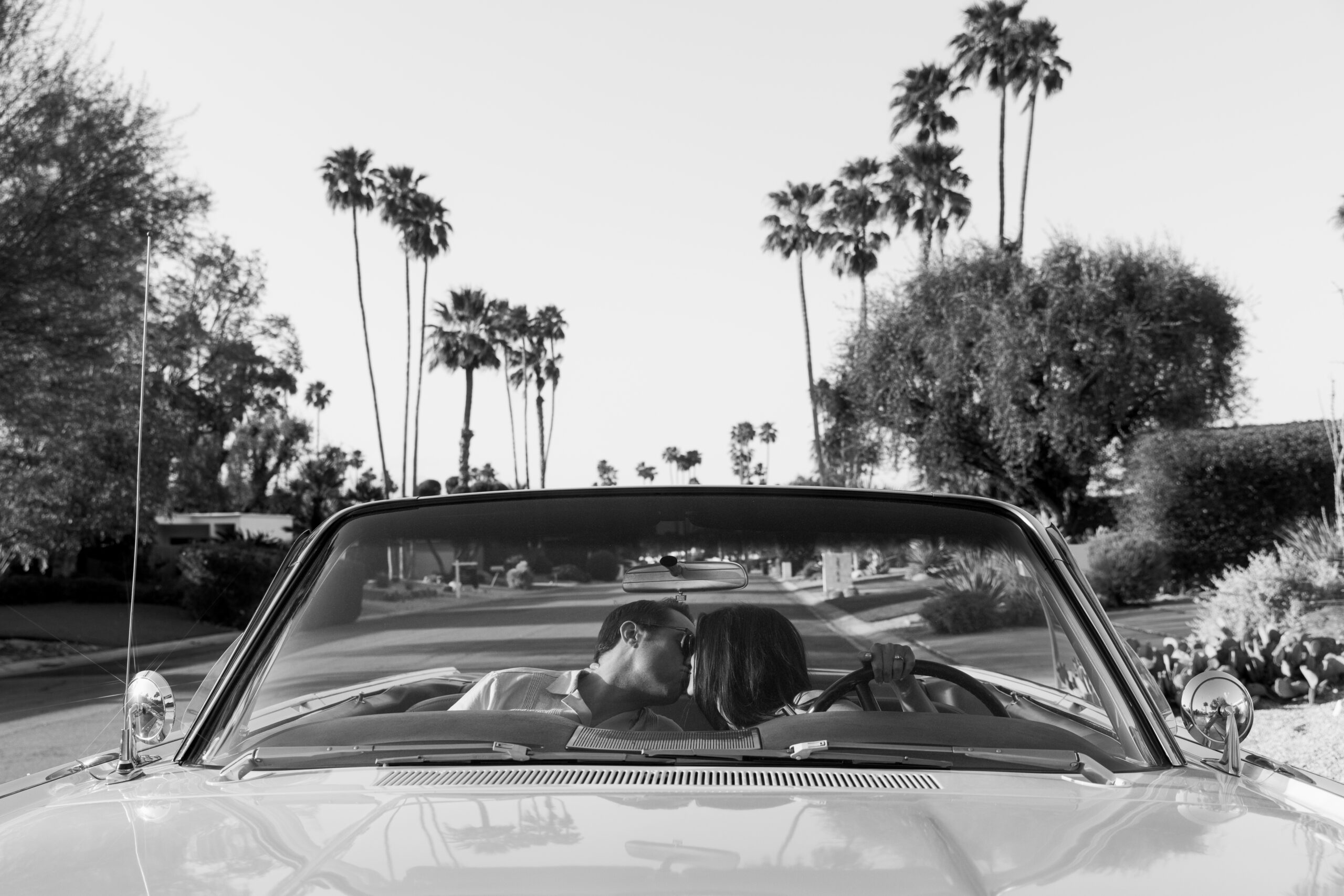 couple kissing in backseat of vintage convertible photographed through windshield with palm trees in the background